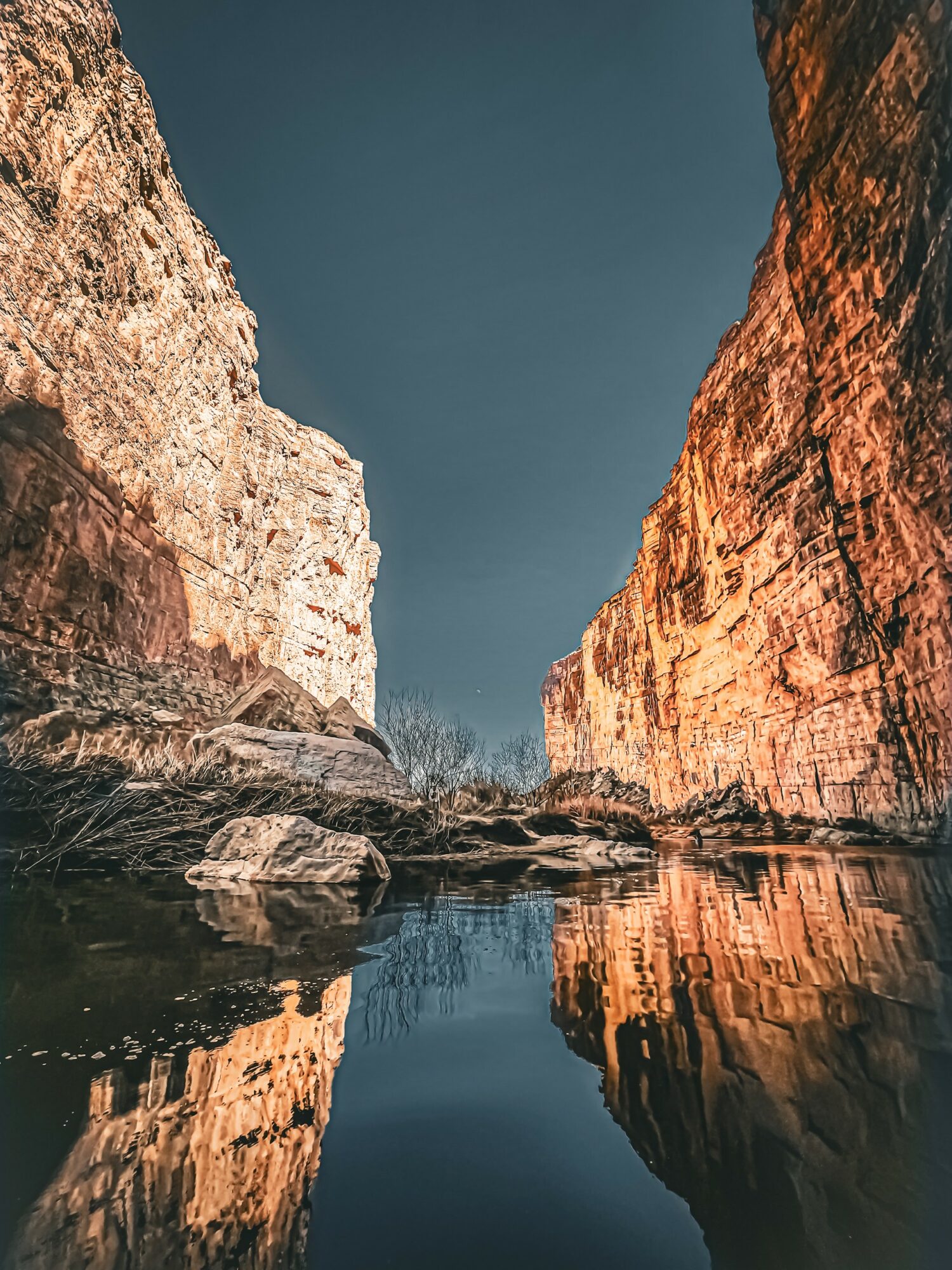 Cliffs on both sides of a calm river with reflections, under a clear sky.