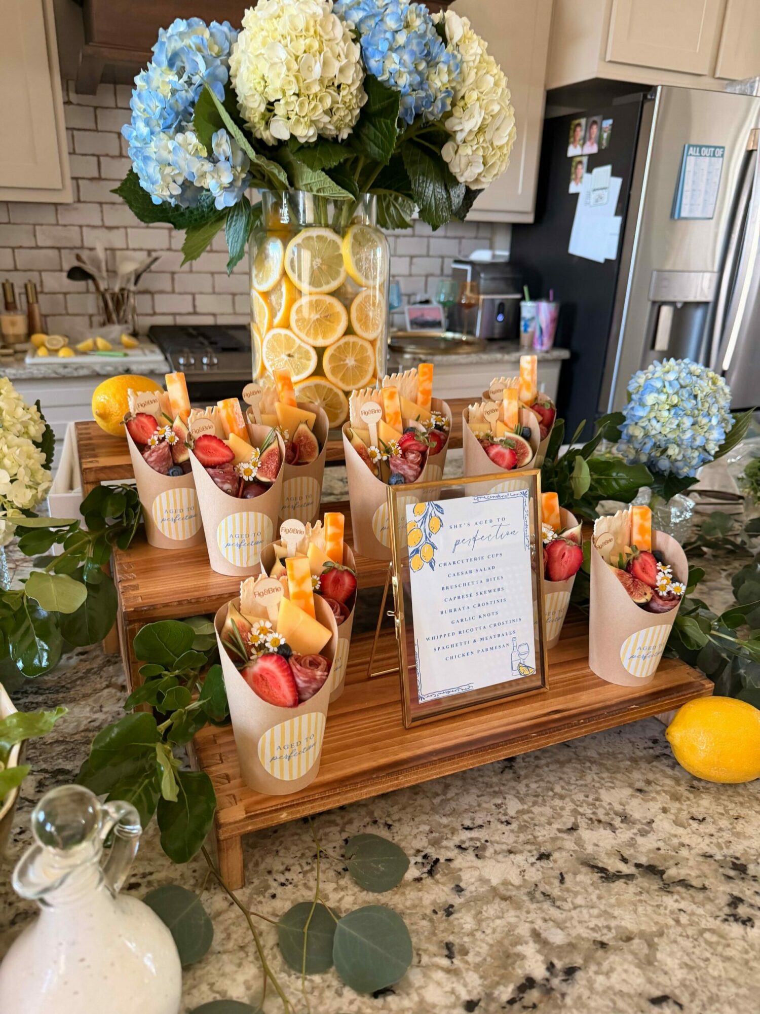 Display of fruit desserts with strawberries, peaches, and whipped cream on a wooden table, decorated with flowers and a framed menu.