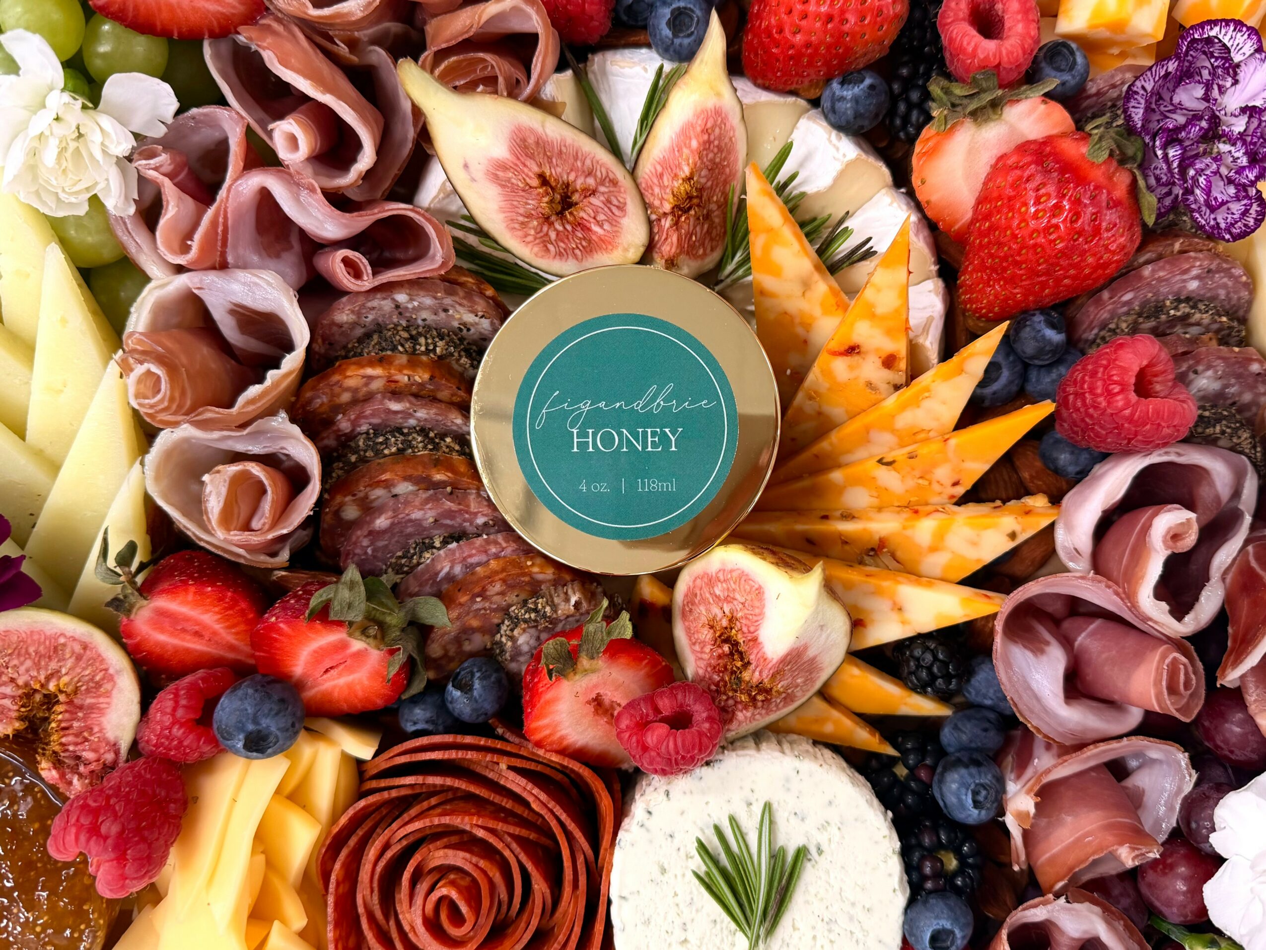 Assorted fruits, cheeses, and cured meats arranged around a honey jar label reading 'signature honey'.