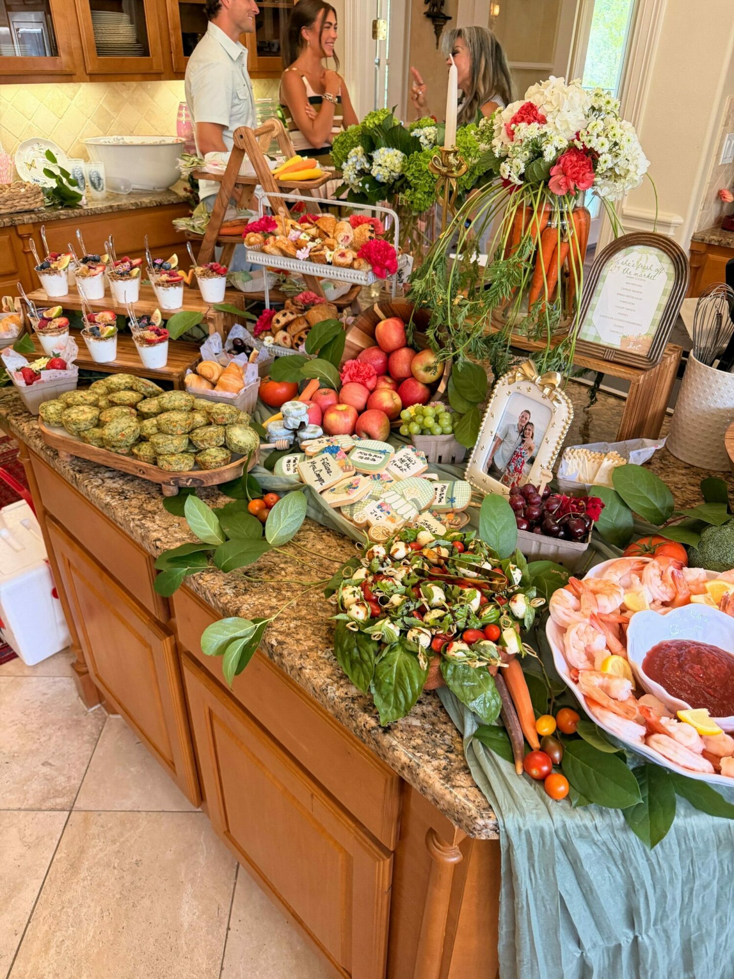 Decorated table with flowers, fruits, and a wreath, featuring photos and various food items, in a home setting.
