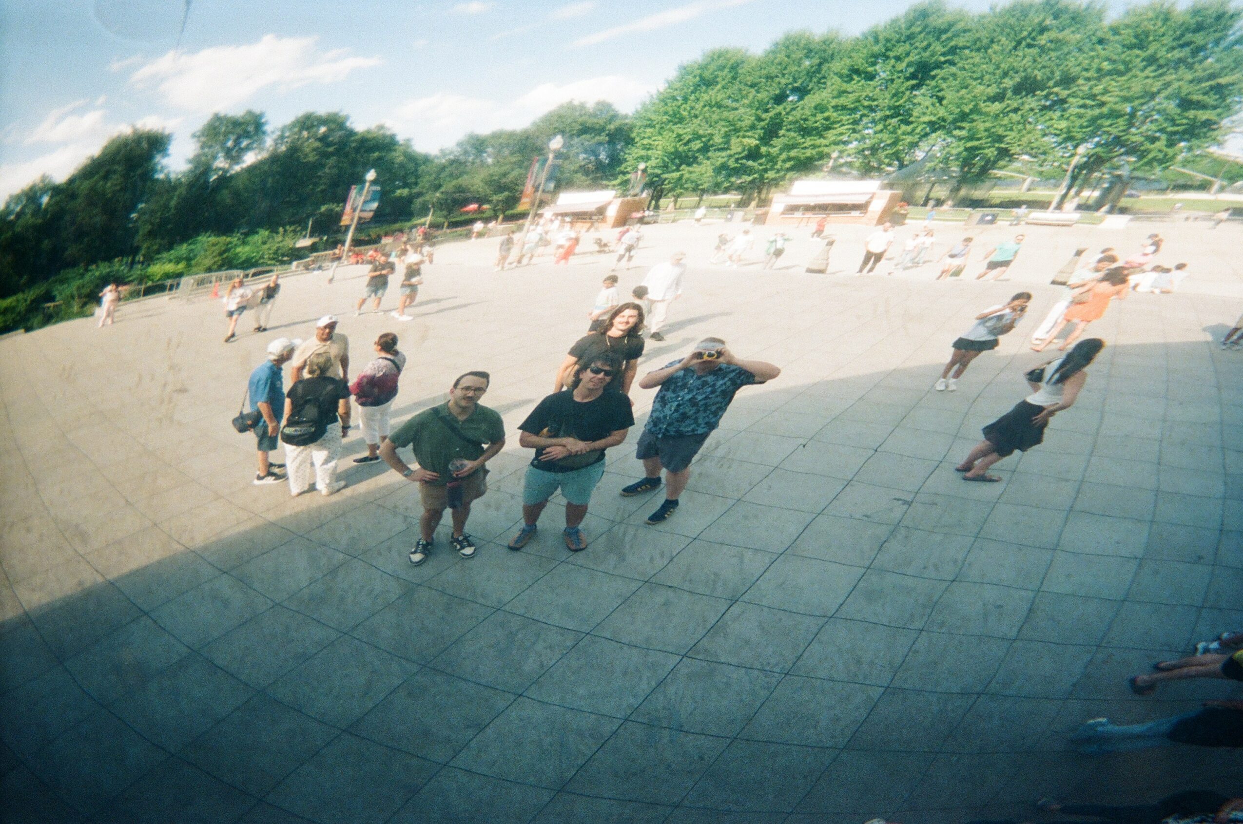 Group of people standing and walking on a tiled outdoor area with trees and sky in background.
