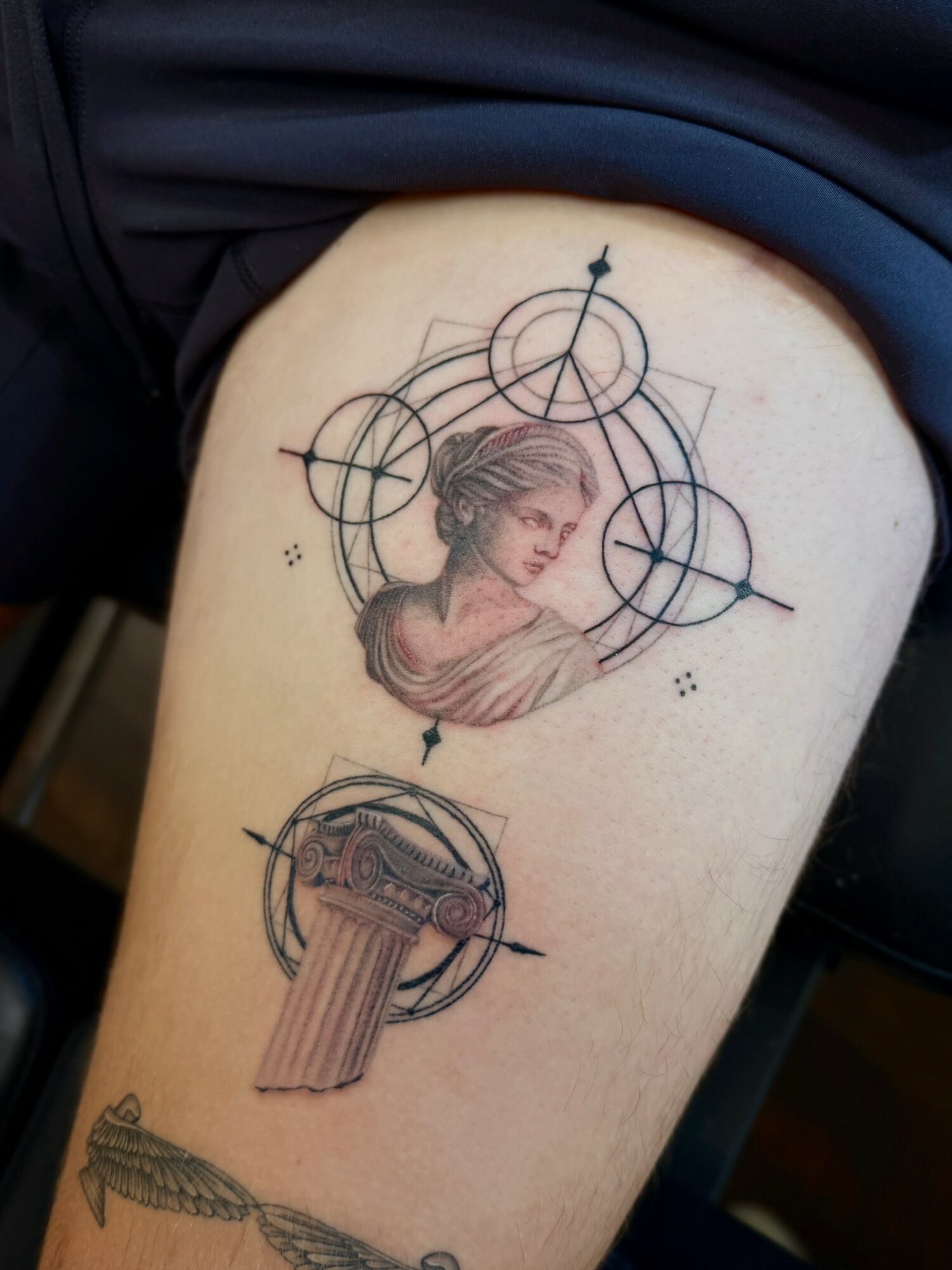 Tattoo of a woman's profile surrounded by geometric circles and lines, with a musical instrument below, on upper thigh.