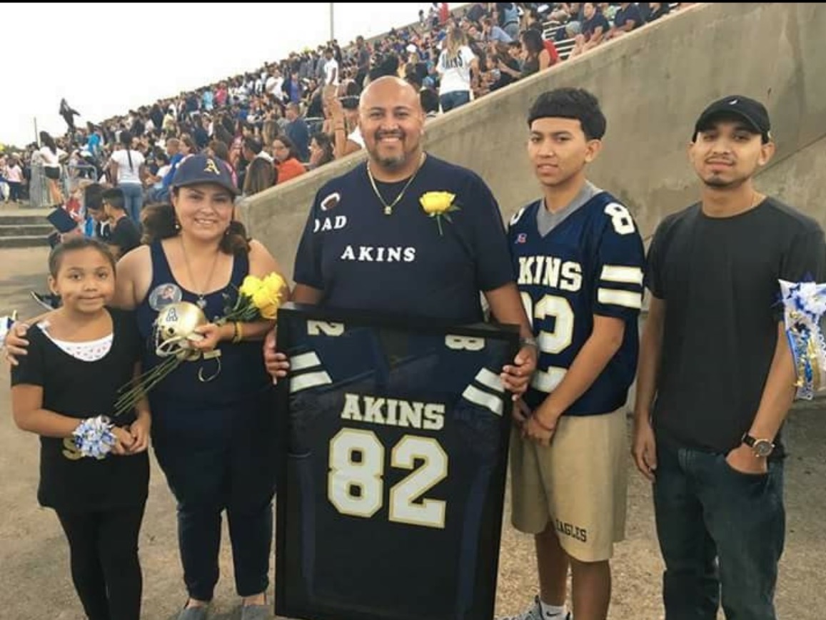 Group of five people, including a man holding a framed sports jersey, standing outdoors with a crowd in the background.