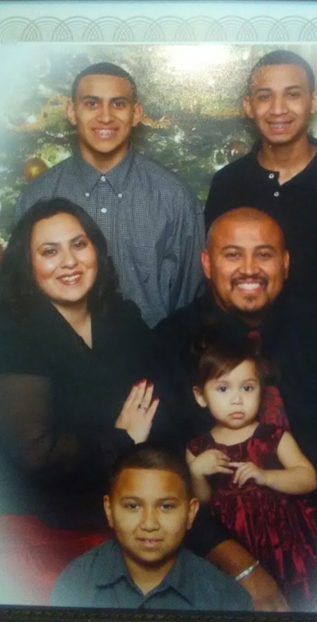 Group of five people, including two children, posing together indoors with a decorative background.
