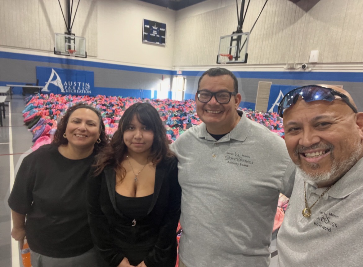 Four people smiling in a gymnasium with a large flower display in the background.