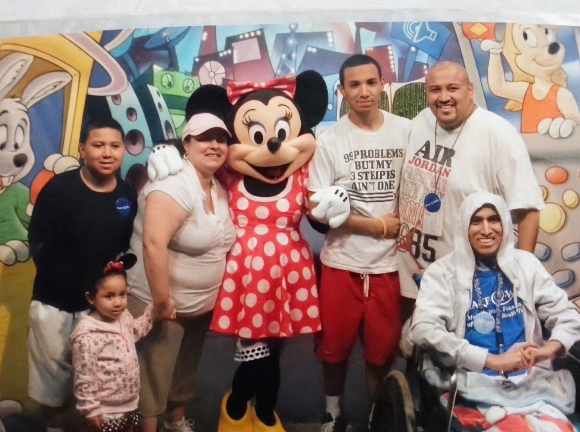 Group of six people, including a person in a Minnie Mouse costume, standing in front of a colorful cartoon-themed background.