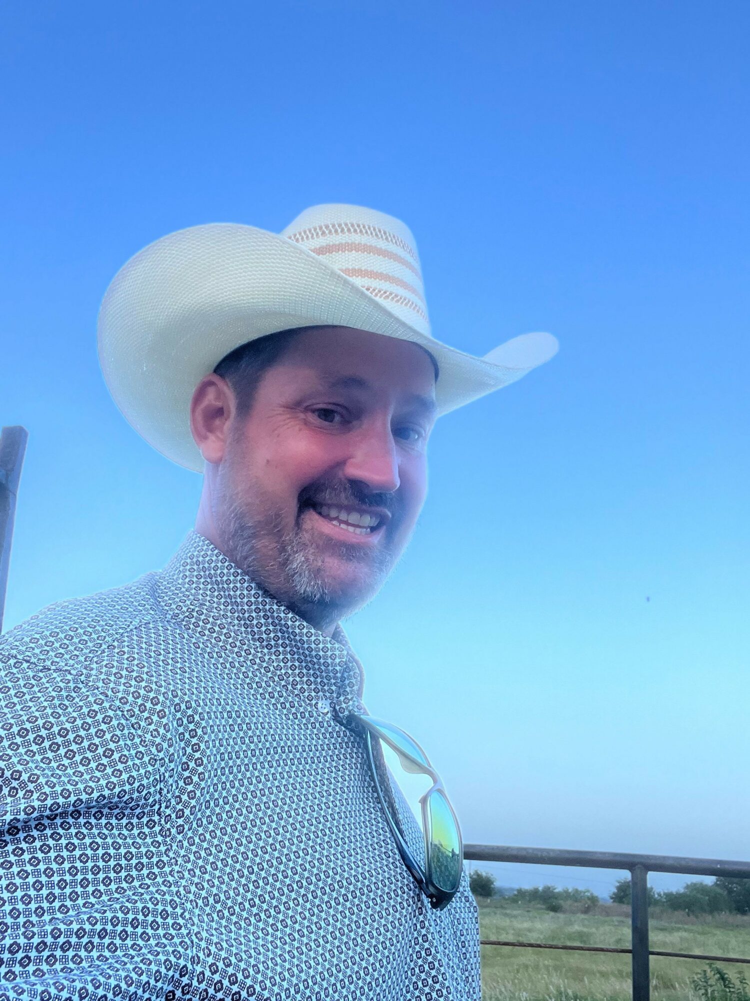 Man wearing a hat and patterned shirt outdoors with a blue sky background.