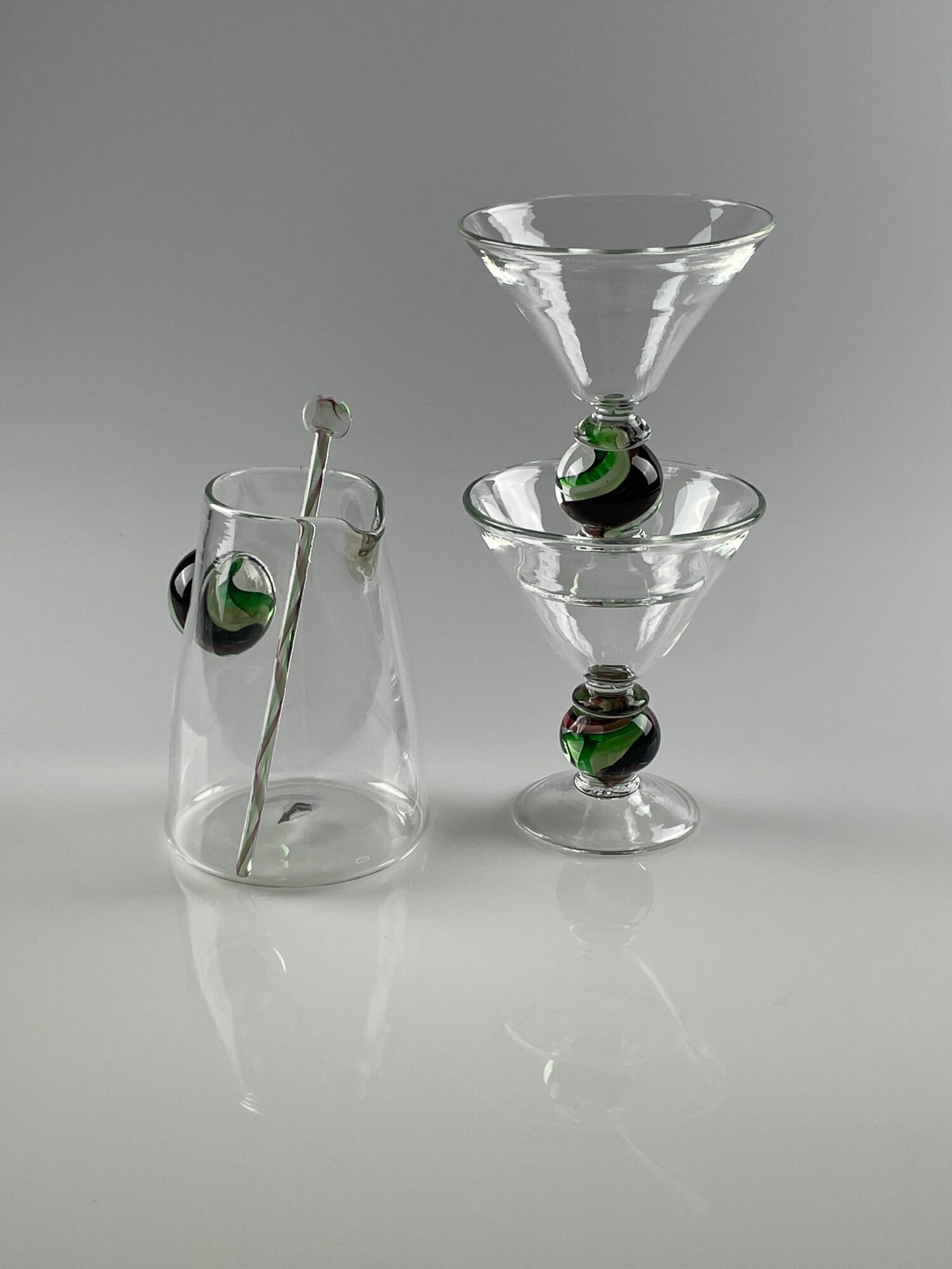 Four upside-down glass objects with black and green details, arranged on a reflective surface, with a plain background.