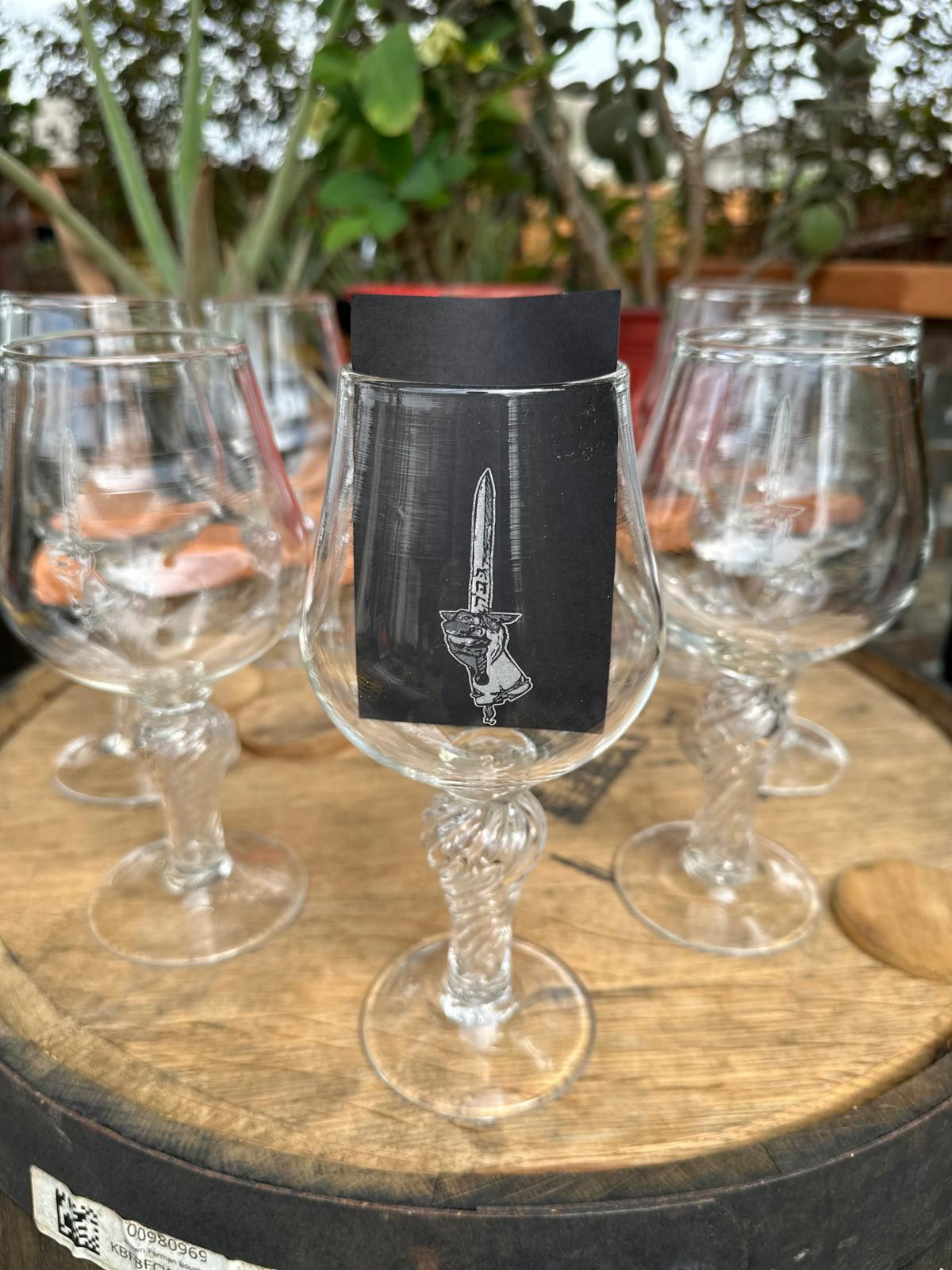 Four empty wine glasses on a wooden table with a black tag featuring a knife illustration hanging from one glass.