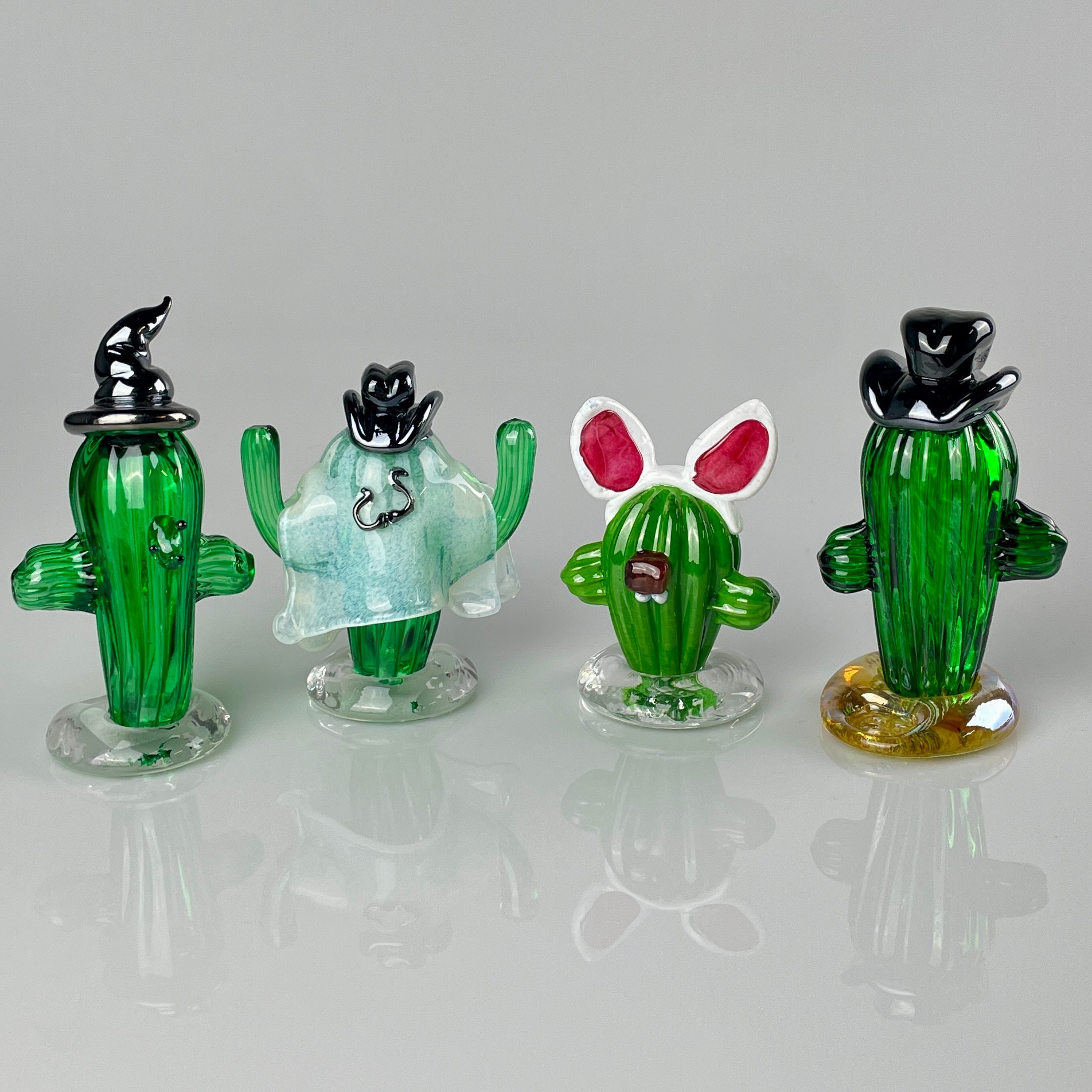 Four glass cactus figurines with animals on top, arranged in a row on a reflective surface.