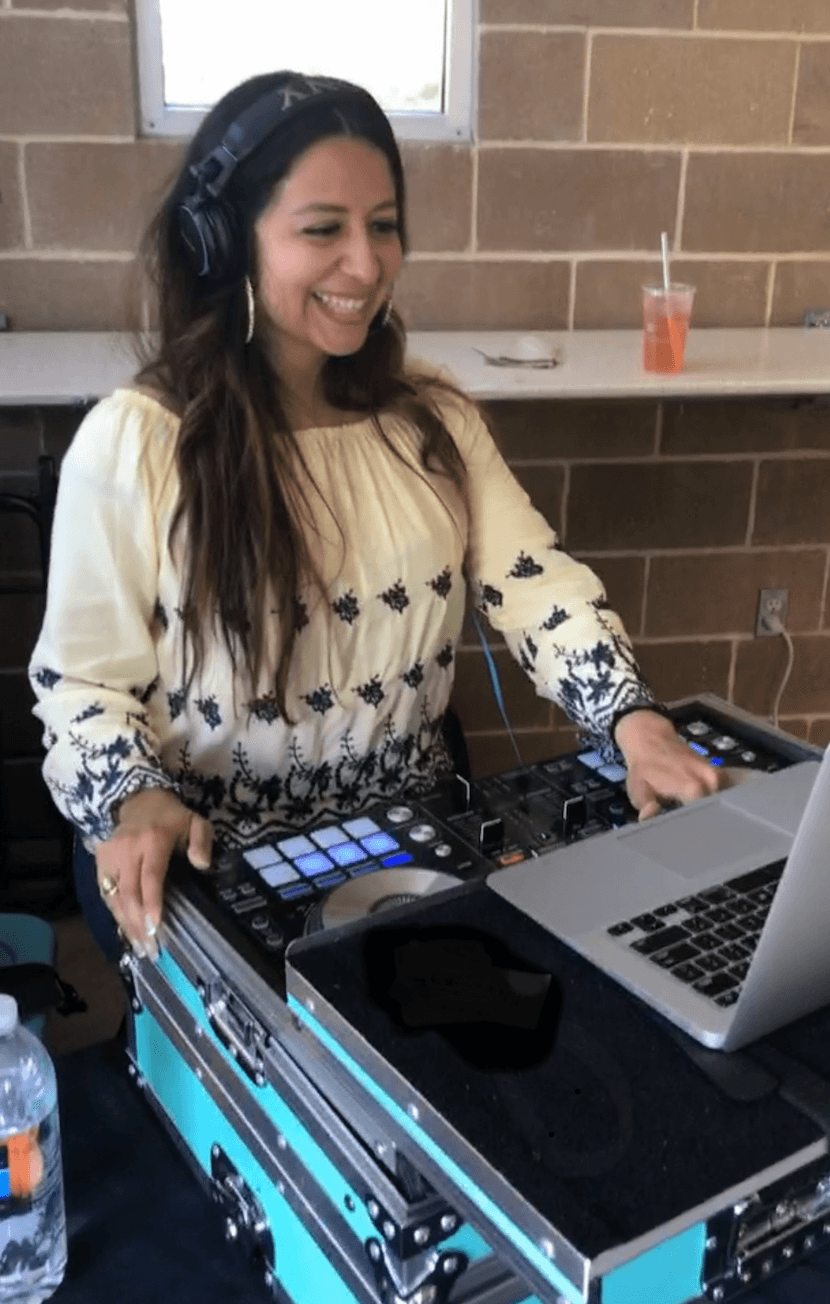 Woman smiling wearing headphones, using DJ equipment and laptop, brick wall background, drink on counter
