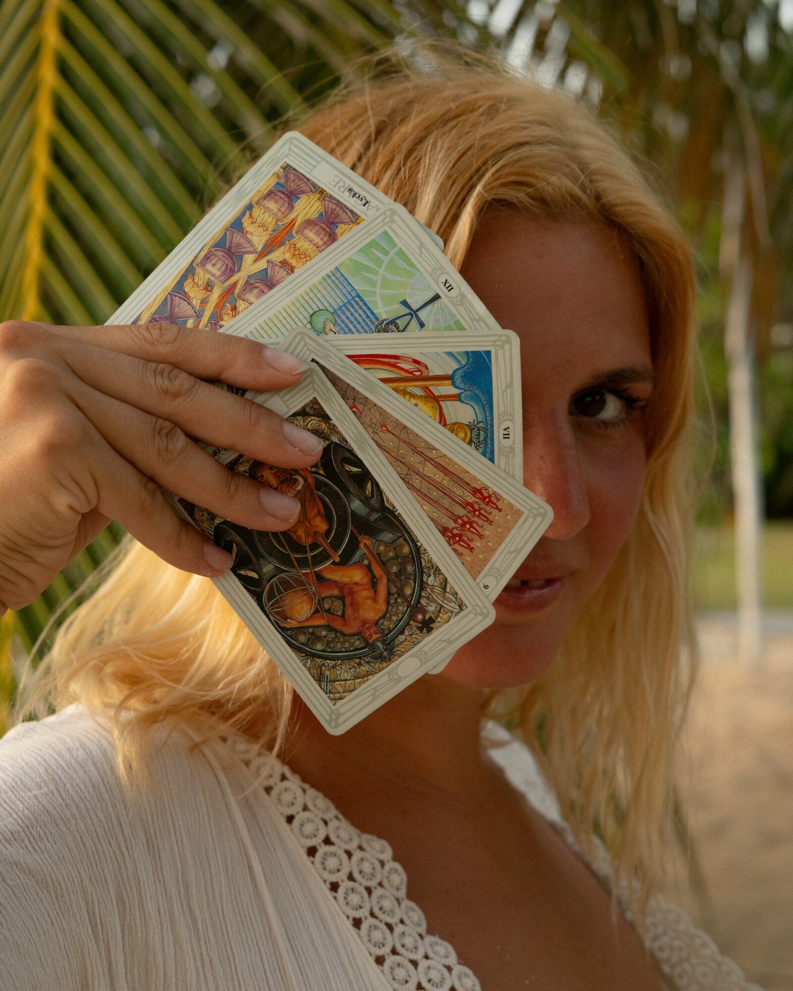 Woman holding a fan of colorful banknotes partially covering her face outdoors, with trees and a fence in the background.
