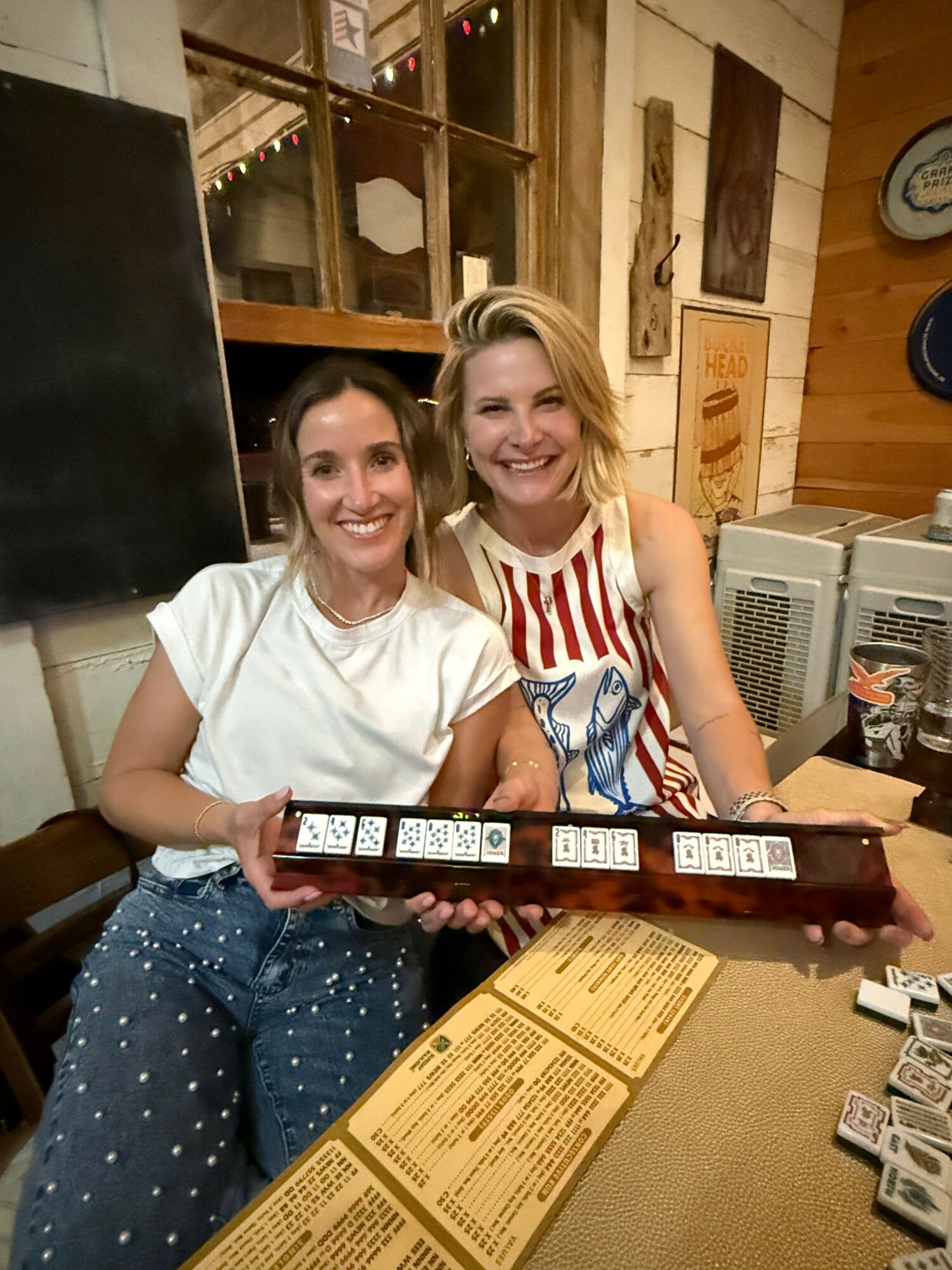Two women sitting at a table, holding a strip of film negatives, smiling at the camera in a cozy indoor setting.