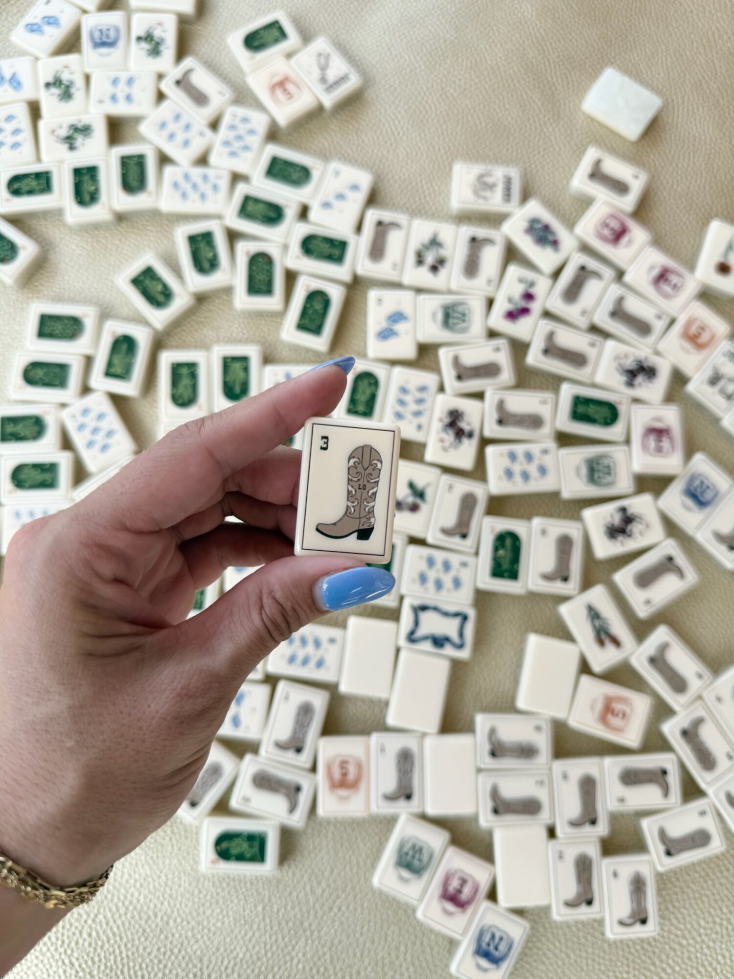 Hand holding a domino tile with a dinosaur illustration, surrounded by scattered domino tiles on a surface.