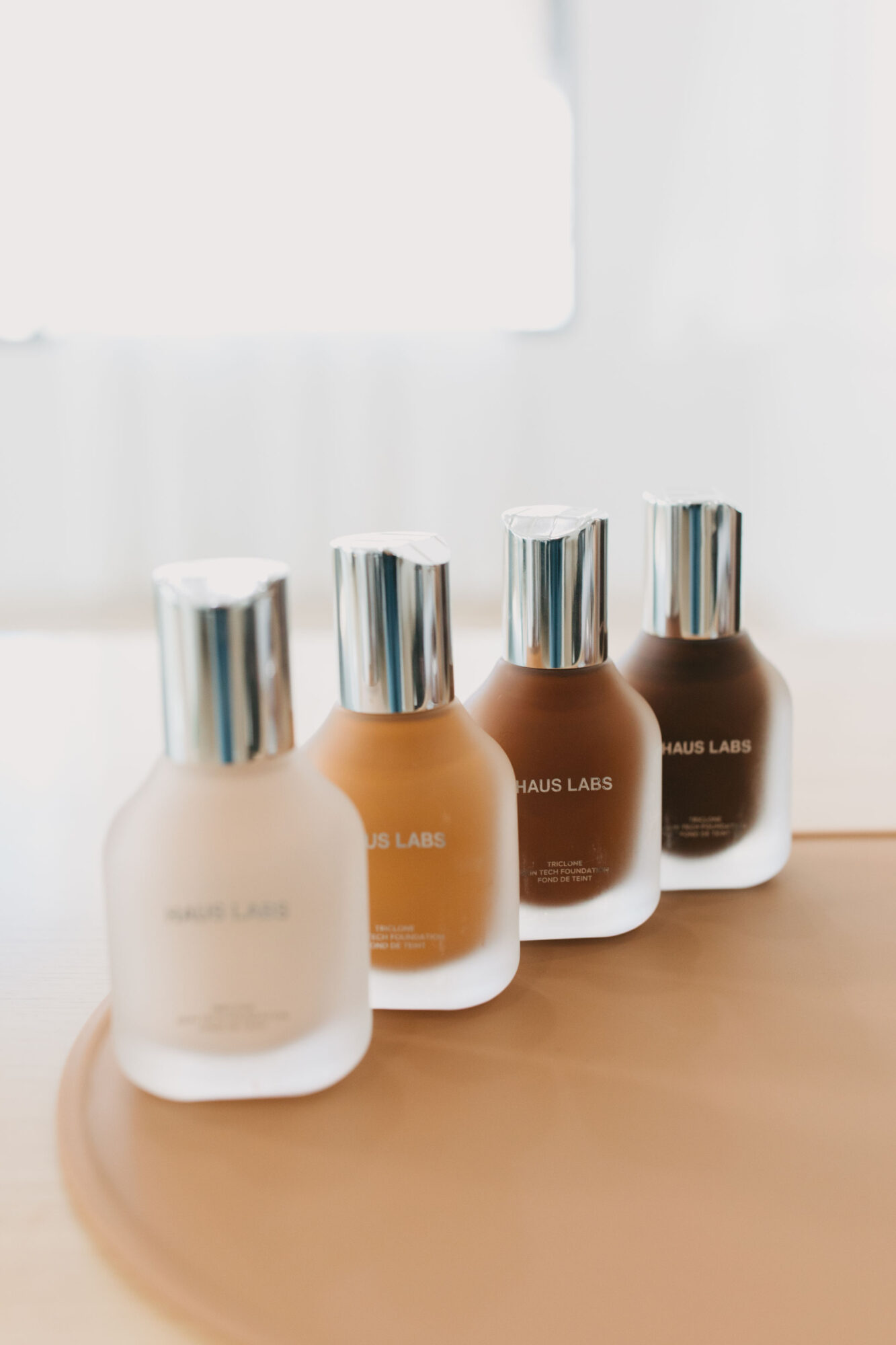 Four bottles with metallic caps arranged in a row on a wooden surface, with a white background.