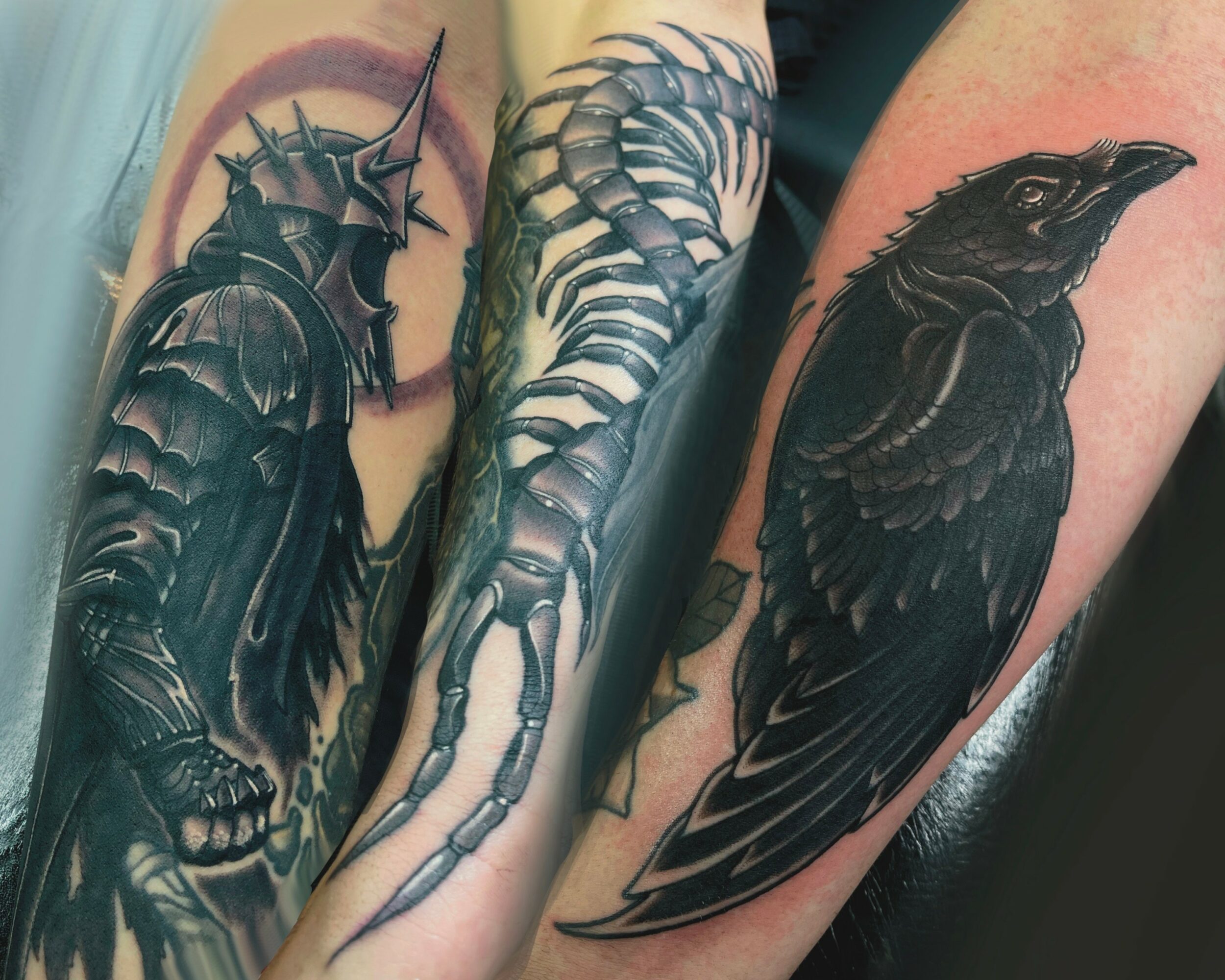 Three tattoos: a knight in armor, a curled skeleton, and a black bird, all in black ink on skin.
