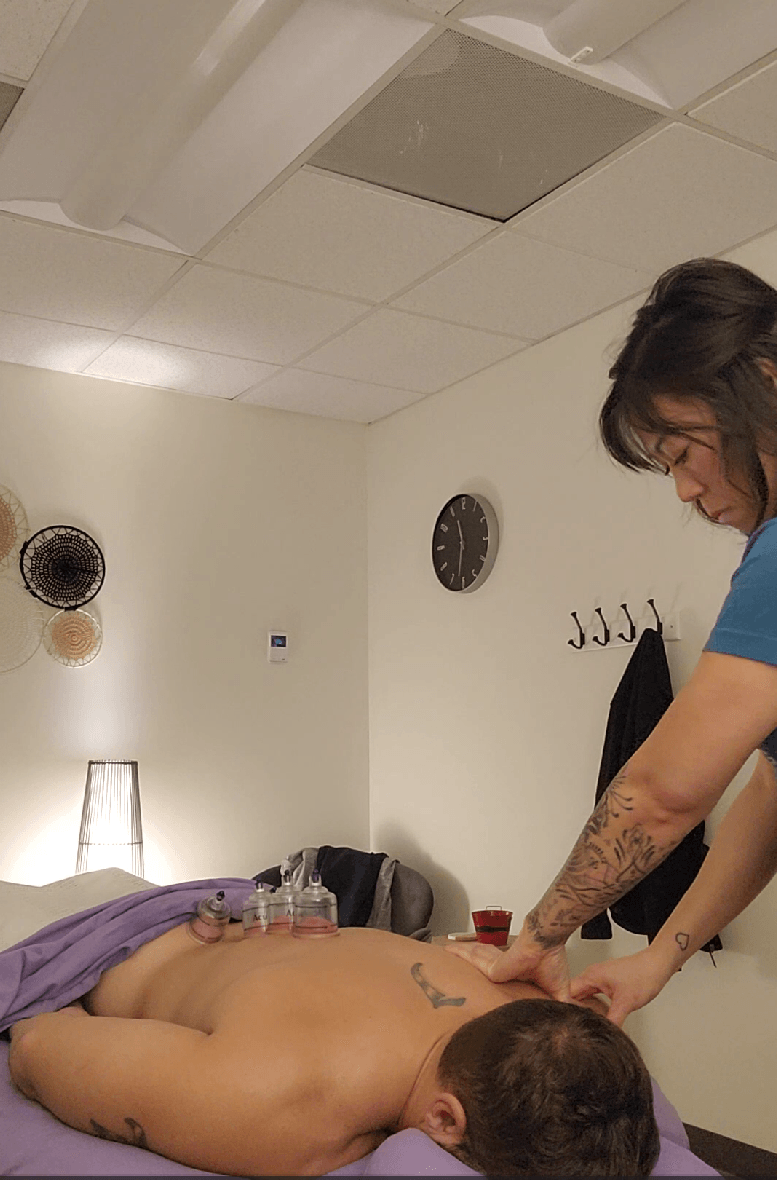 Person receiving a massage from a therapist in a room with a clock and wall hooks, dim lighting.