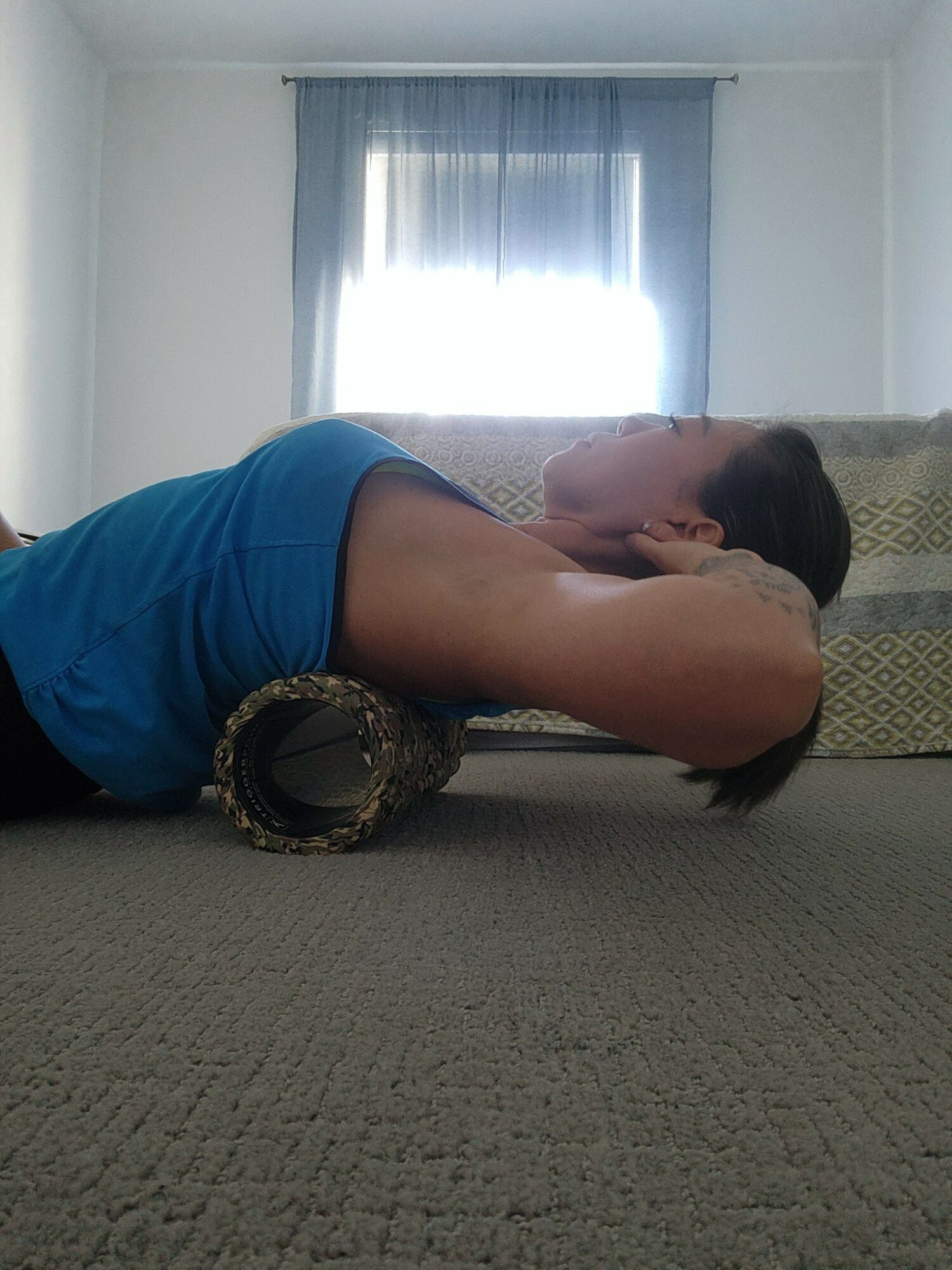 Person lying on side on carpeted floor in a room with window and blinds, facing away from camera.