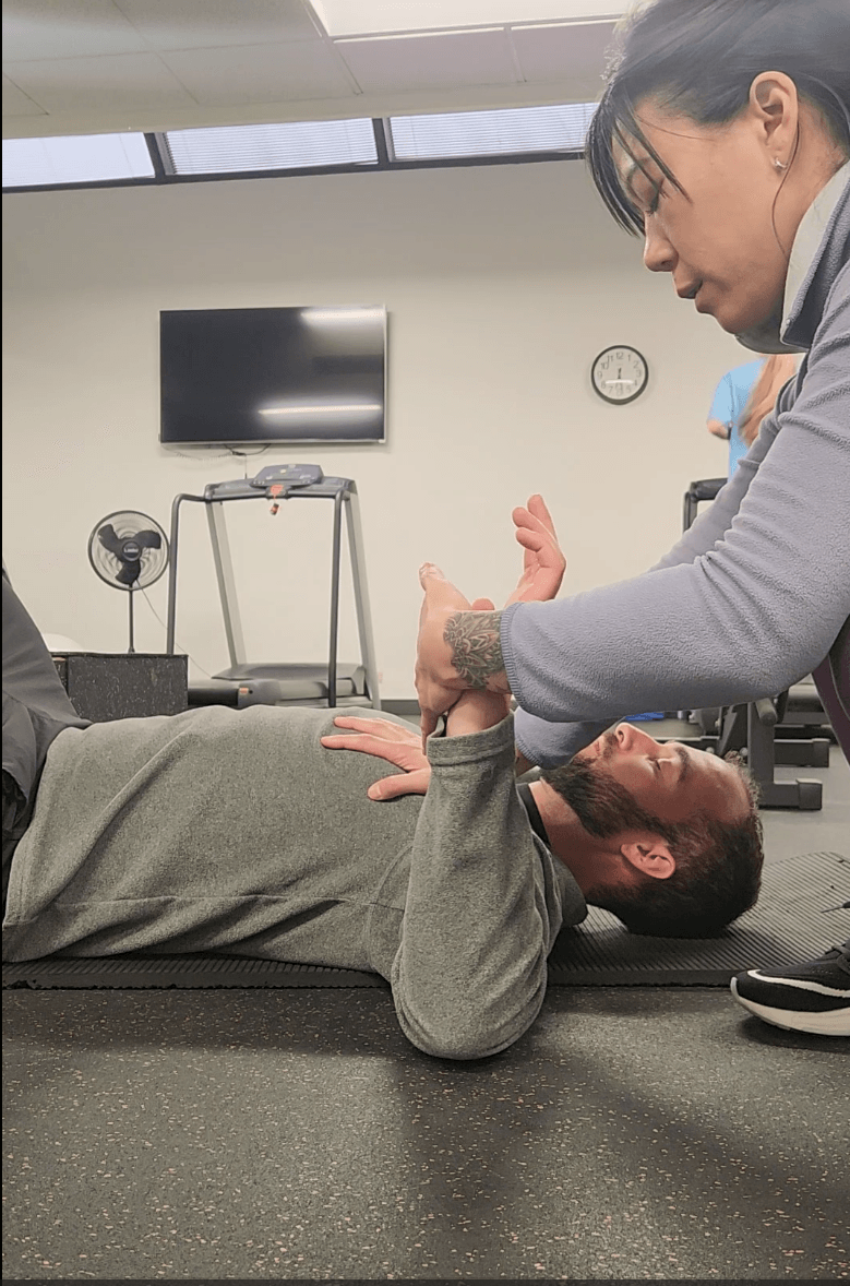 A person lying on the floor receiving assistance from a woman, in a room with a TV and clock on the wall.