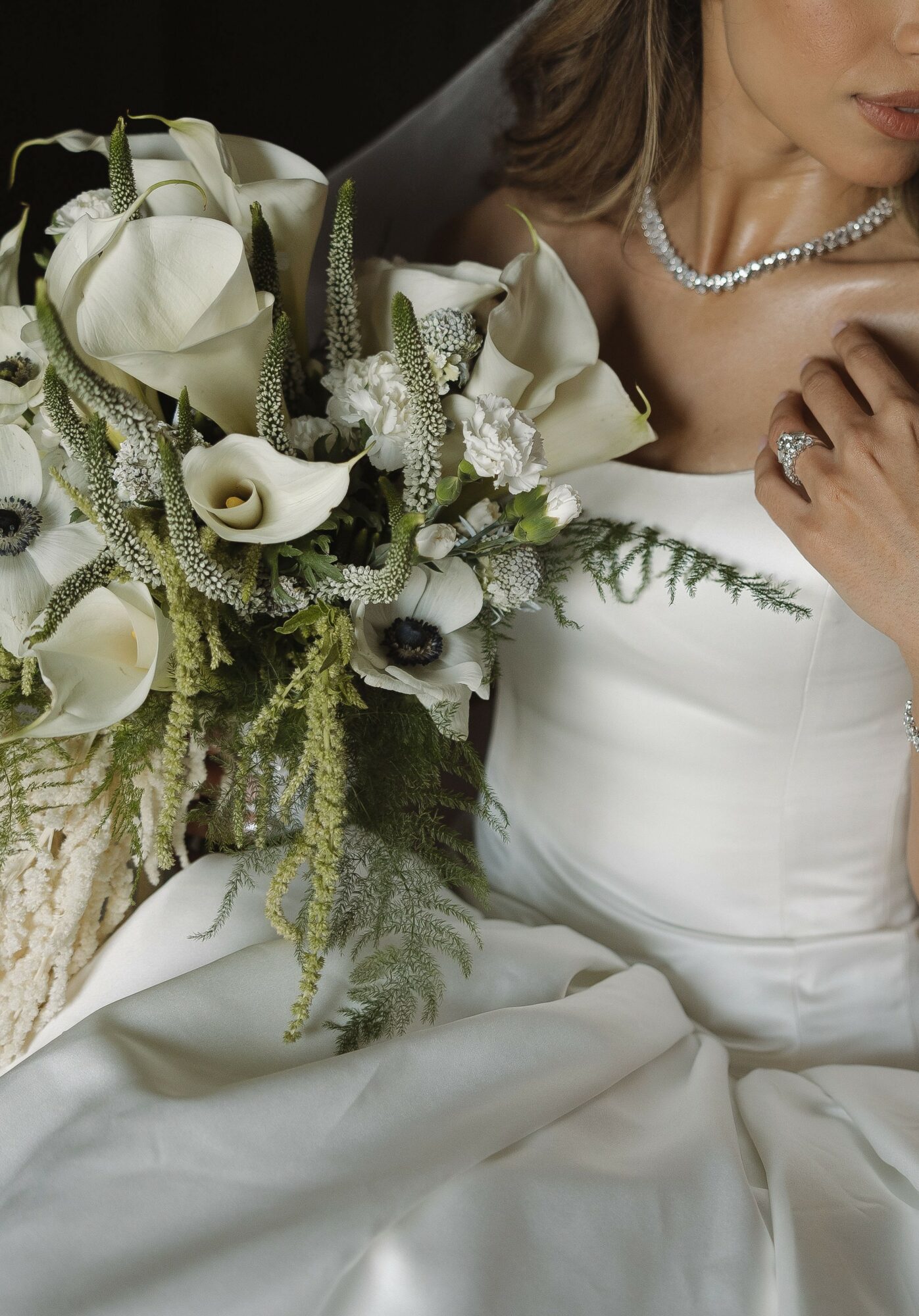 Close-up of a bride holding a large bouquet of white flowers, wearing a white dress and pearl necklace.