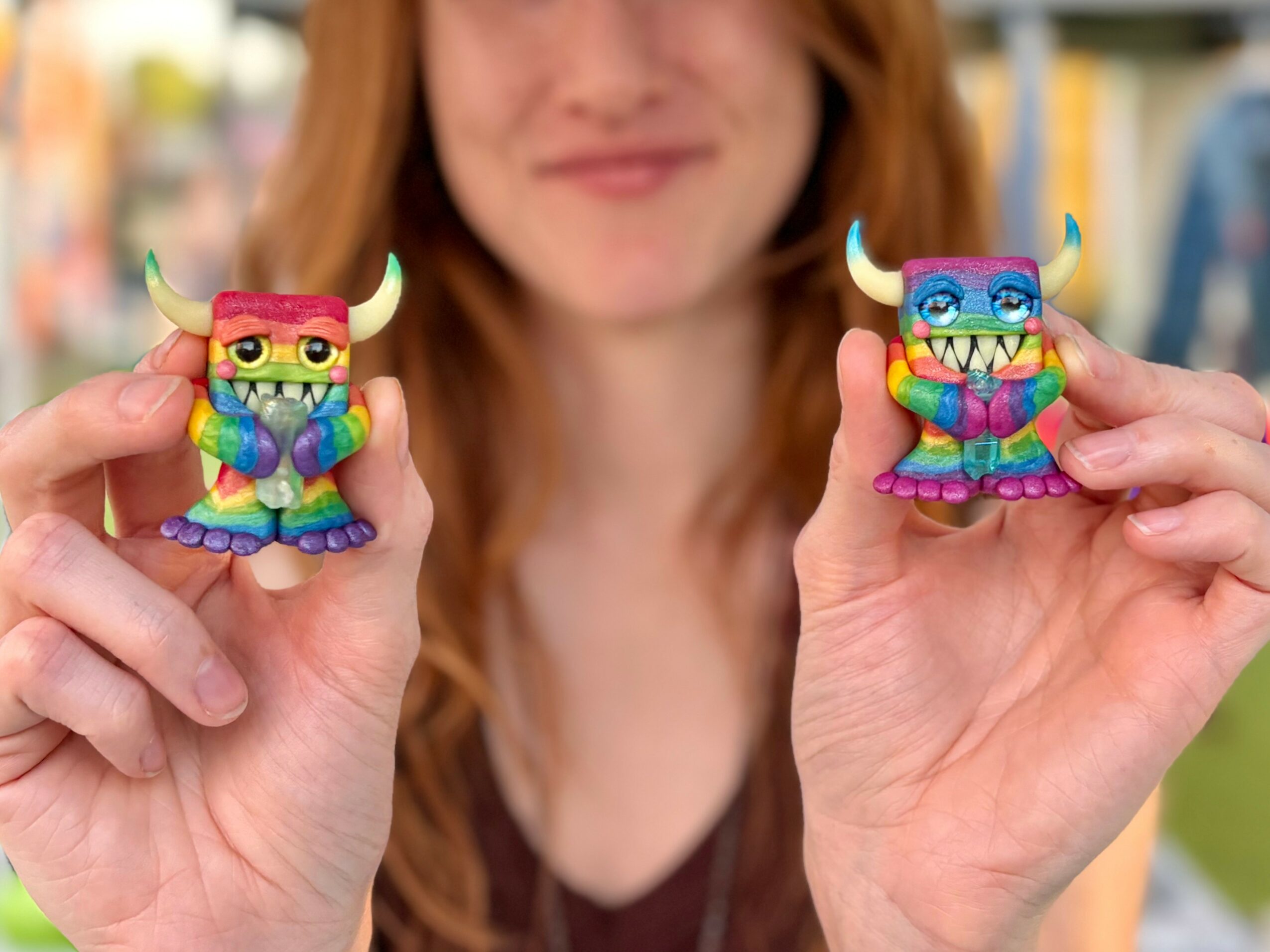 Person holding two colorful monster figurines, smiling, with blurred background.