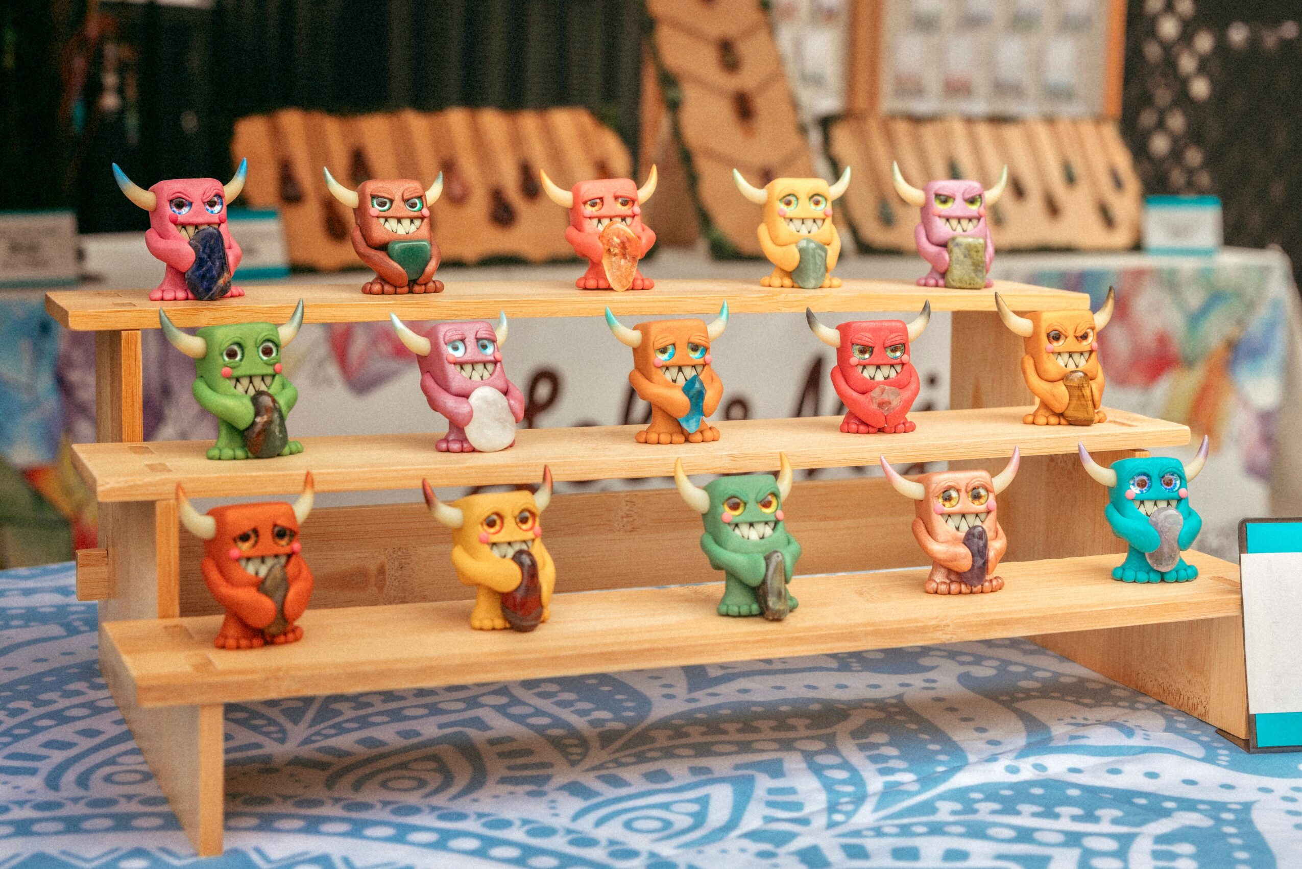 Three-tier wooden display shelf with colorful toy animals, set on a patterned blue tablecloth, with blurred background.