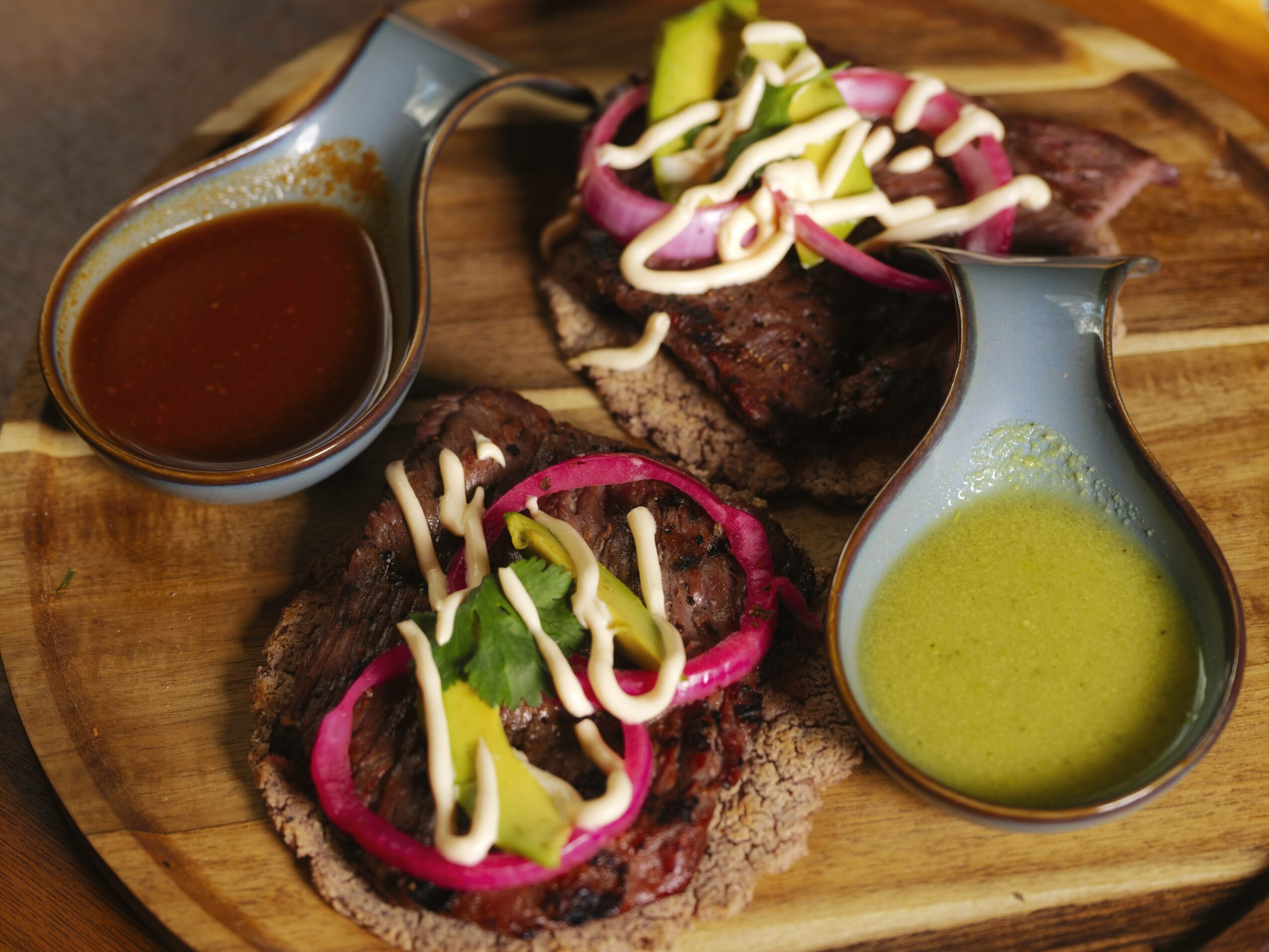 Two pieces of grilled meat topped with pickled vegetables and sauces on a wooden serving board.