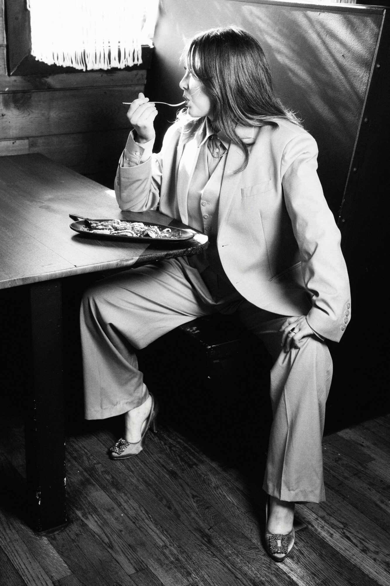 Woman sitting at a table, eating, with a tray of food, in a black-and-white setting.