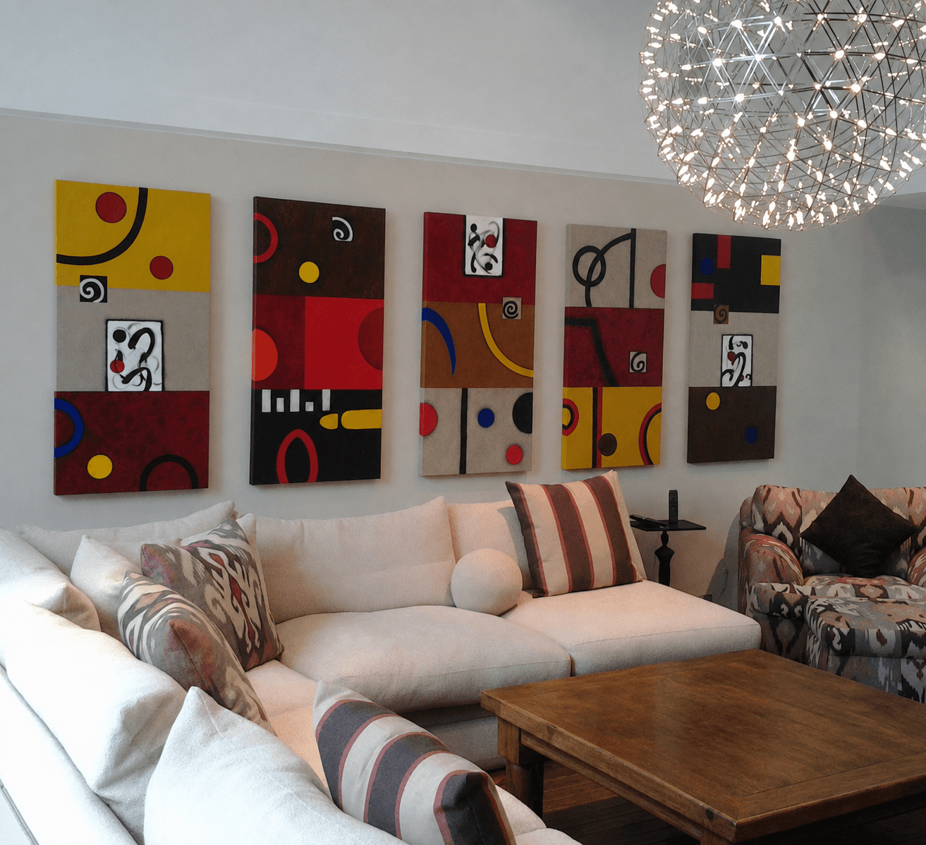 Living room with abstract artwork on the wall, white sofa with patterned pillows, wooden coffee table, and a chandelier.