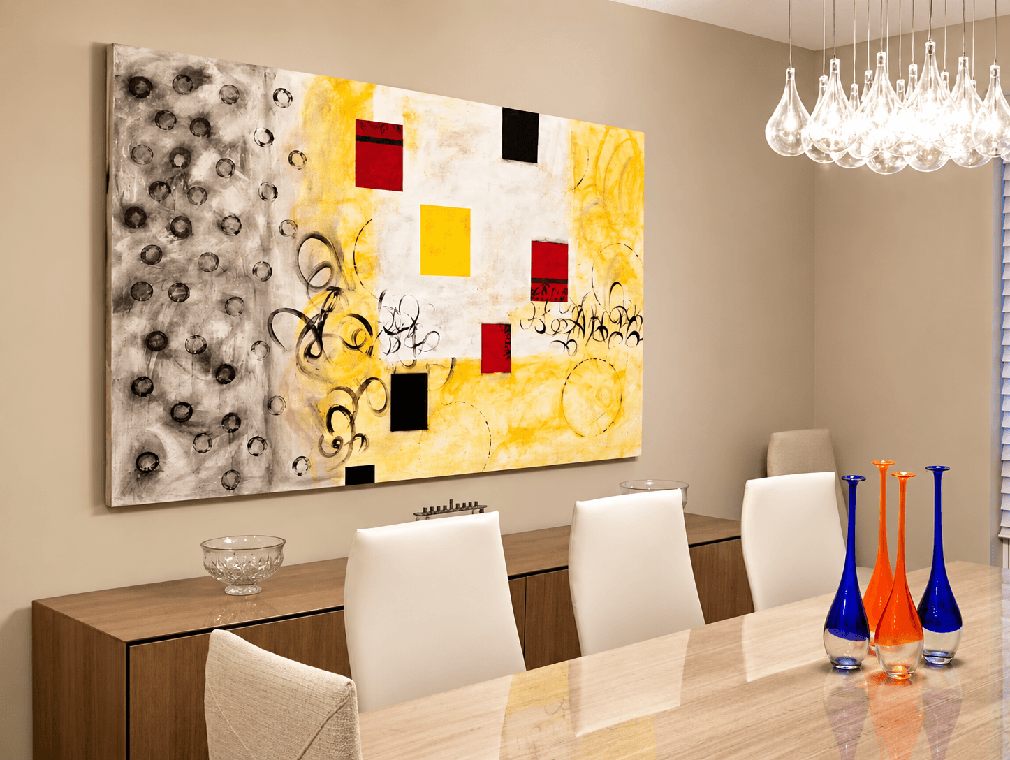 Modern dining room with a large abstract painting, white chairs, a wooden table, and colorful vases, chandelier overhead.