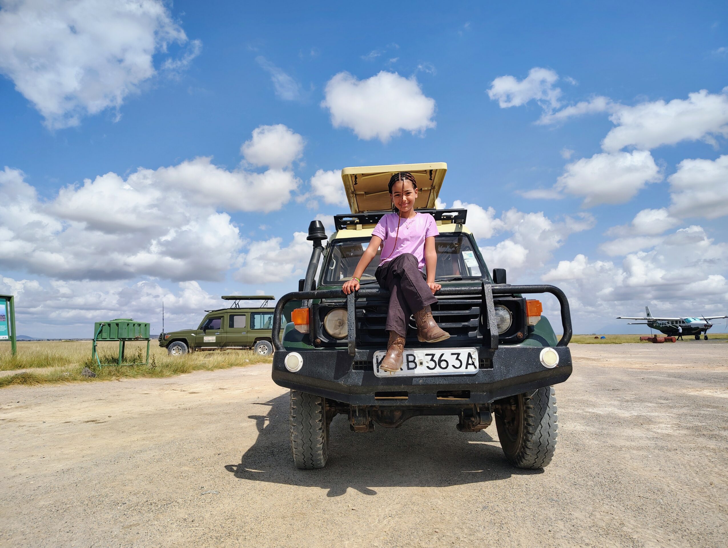 Person standing on front of a vehicle outdoors under a blue sky with clouds.