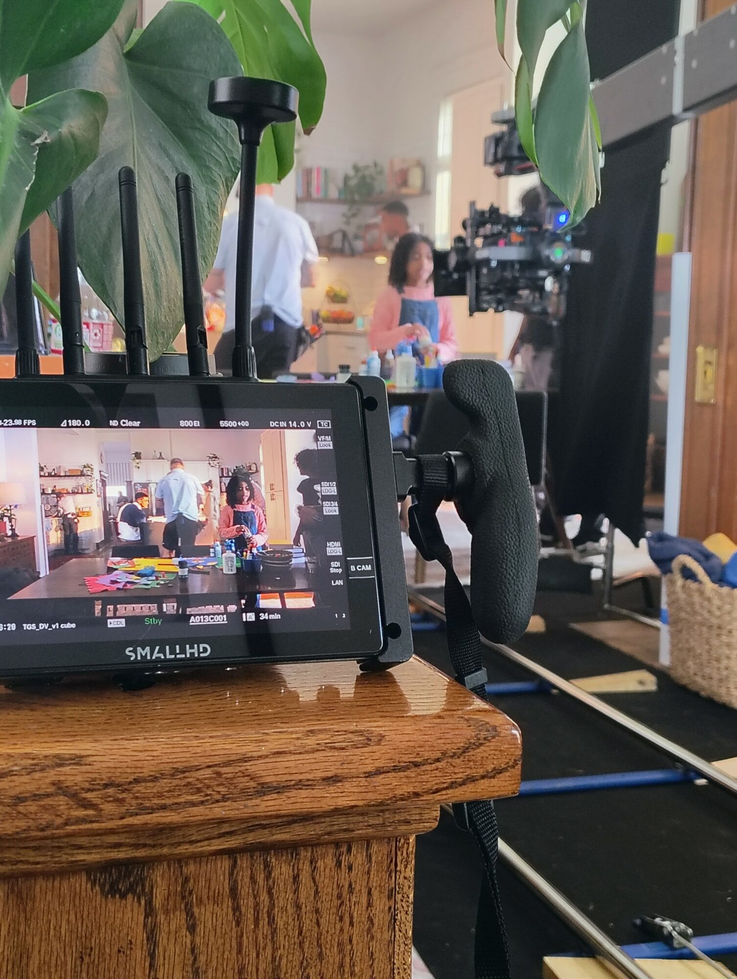 Camera monitor on a wooden table records a scene with people and a camera setup in a room.