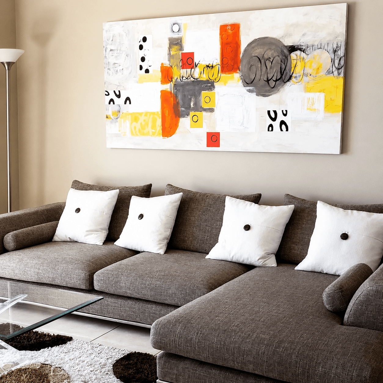Living room with a gray sofa, white pillows, a glass coffee table, a large abstract painting, and a beige wall.