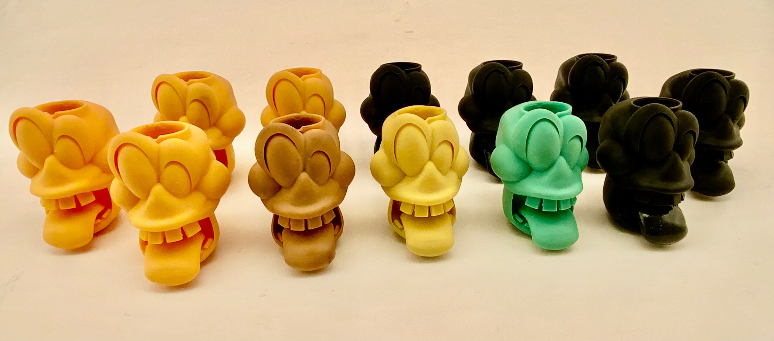 Six small figurines in yellow, brown, yellow, green, and black, arranged in a row on a white surface.
