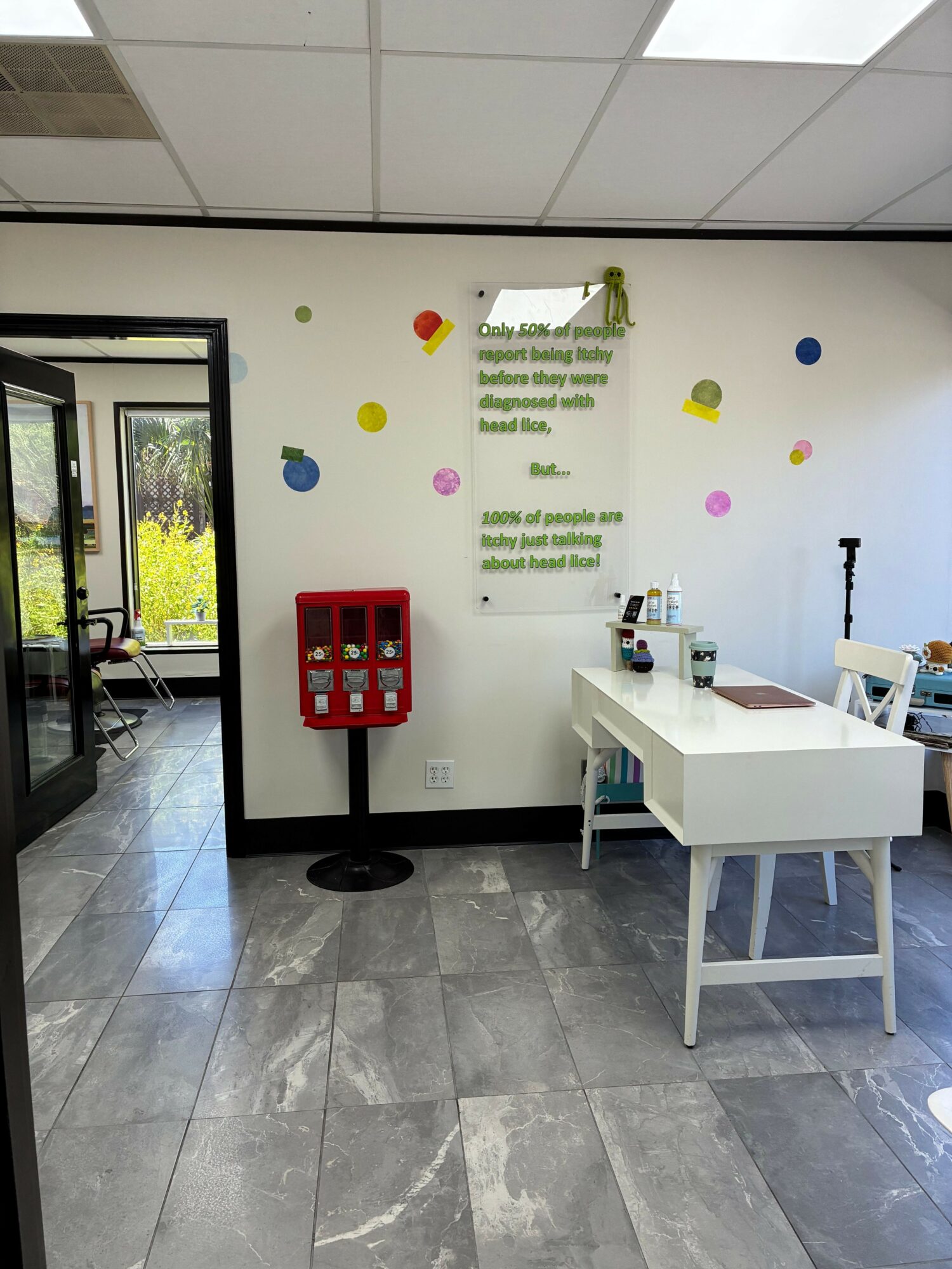 Office space with a white desk, colorful wall decorations, and a red cabinet, viewed through a glass door.