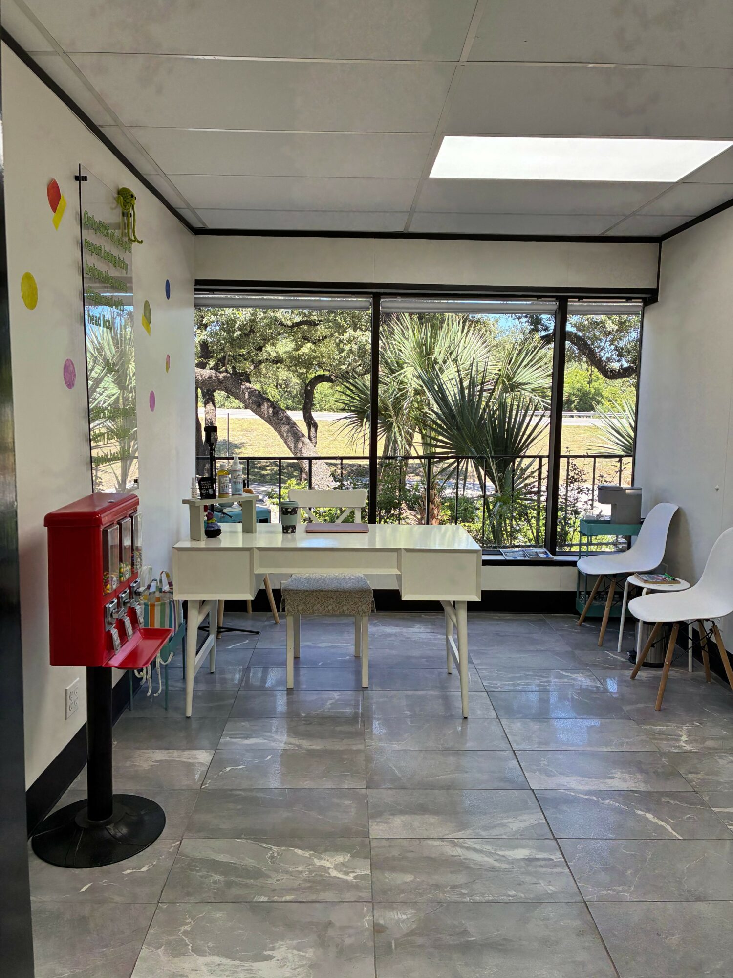 Room with large windows, white chairs, a table, and a red fire extinguisher on a stand, with trees outside.