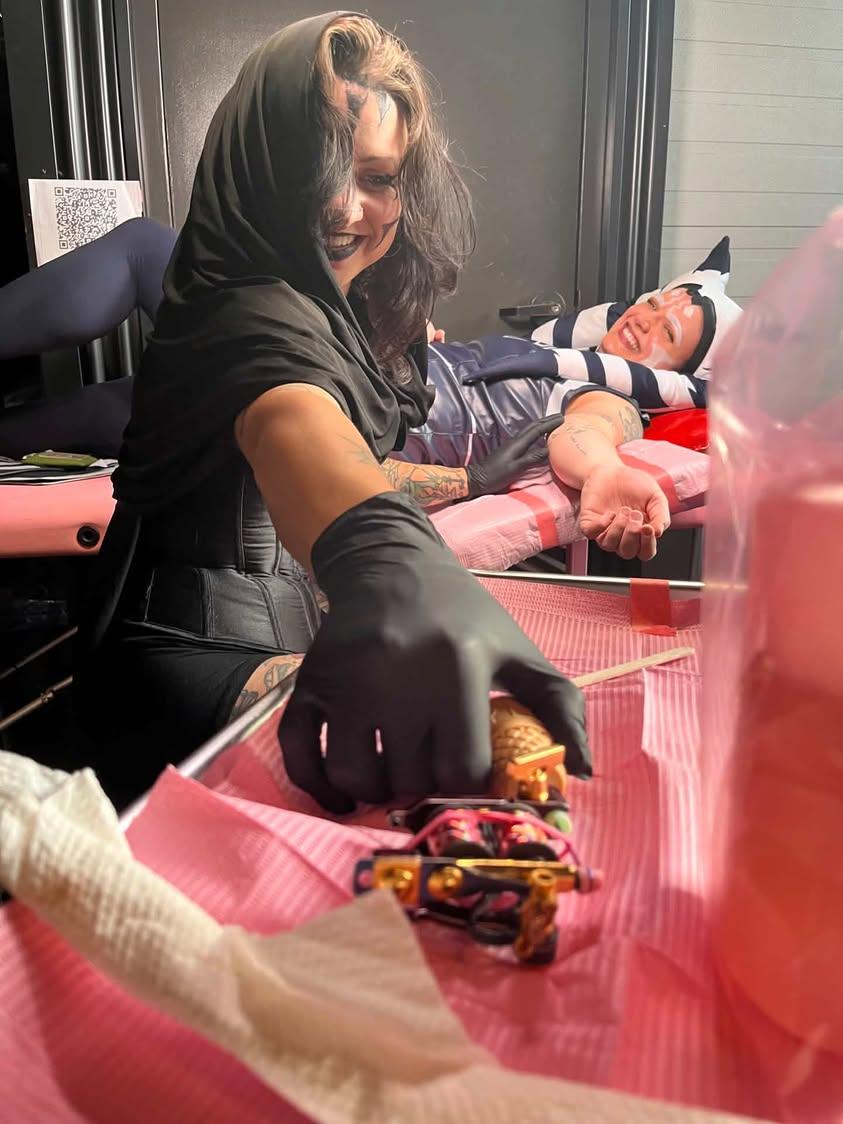Woman wearing black gloves and a headscarf preparing items on a table, with a person lying on a bed in the background.