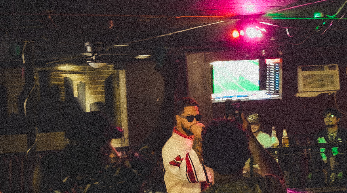 Person singing into a microphone in a dimly lit bar with other people present.