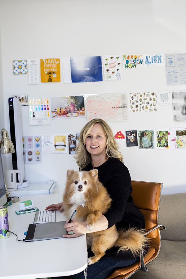 Woman sitting at desk holding a small dog in an office with posters on the wall behind her.
