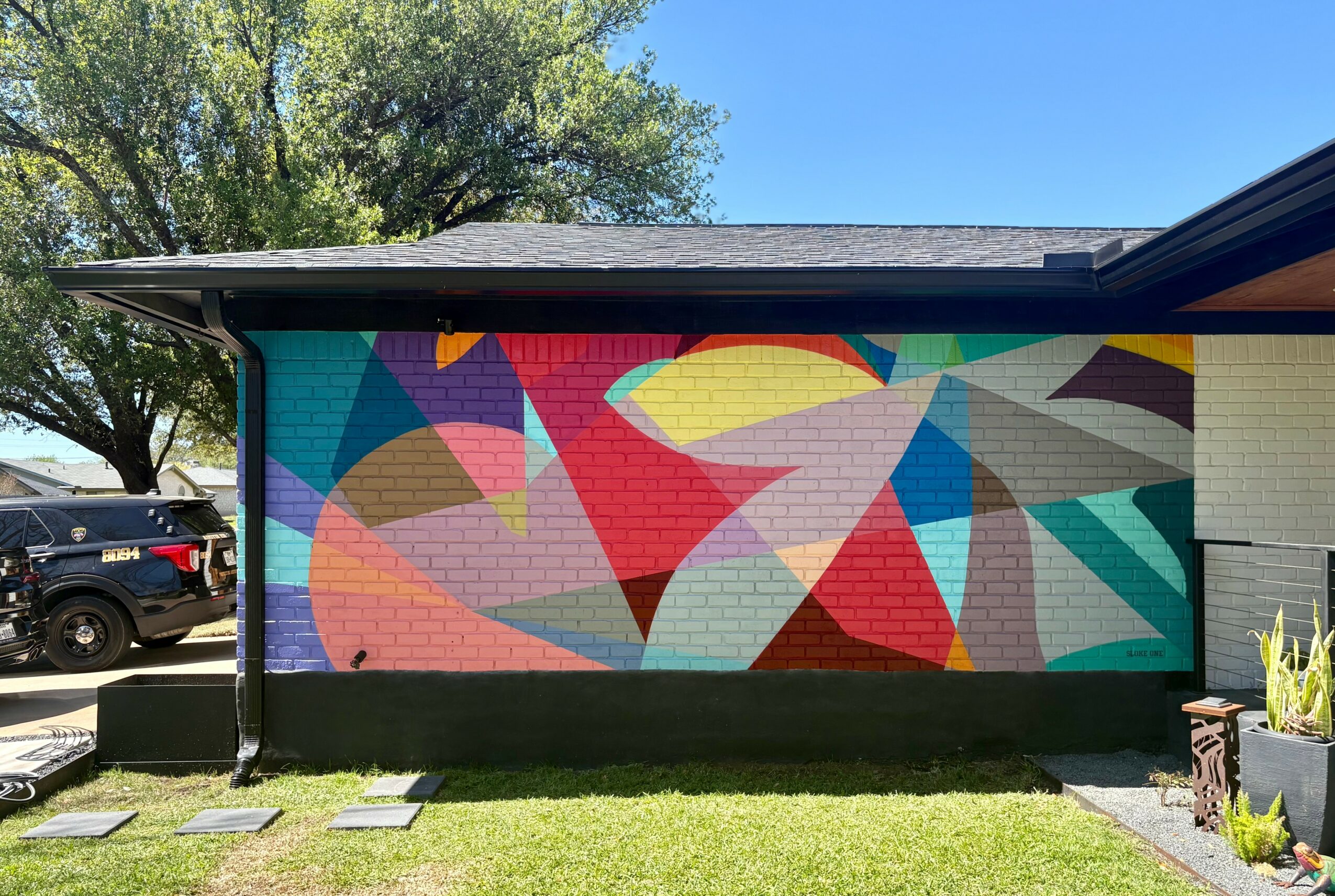 Colorful abstract mural on building wall with various shapes and bright colors, under a clear blue sky.