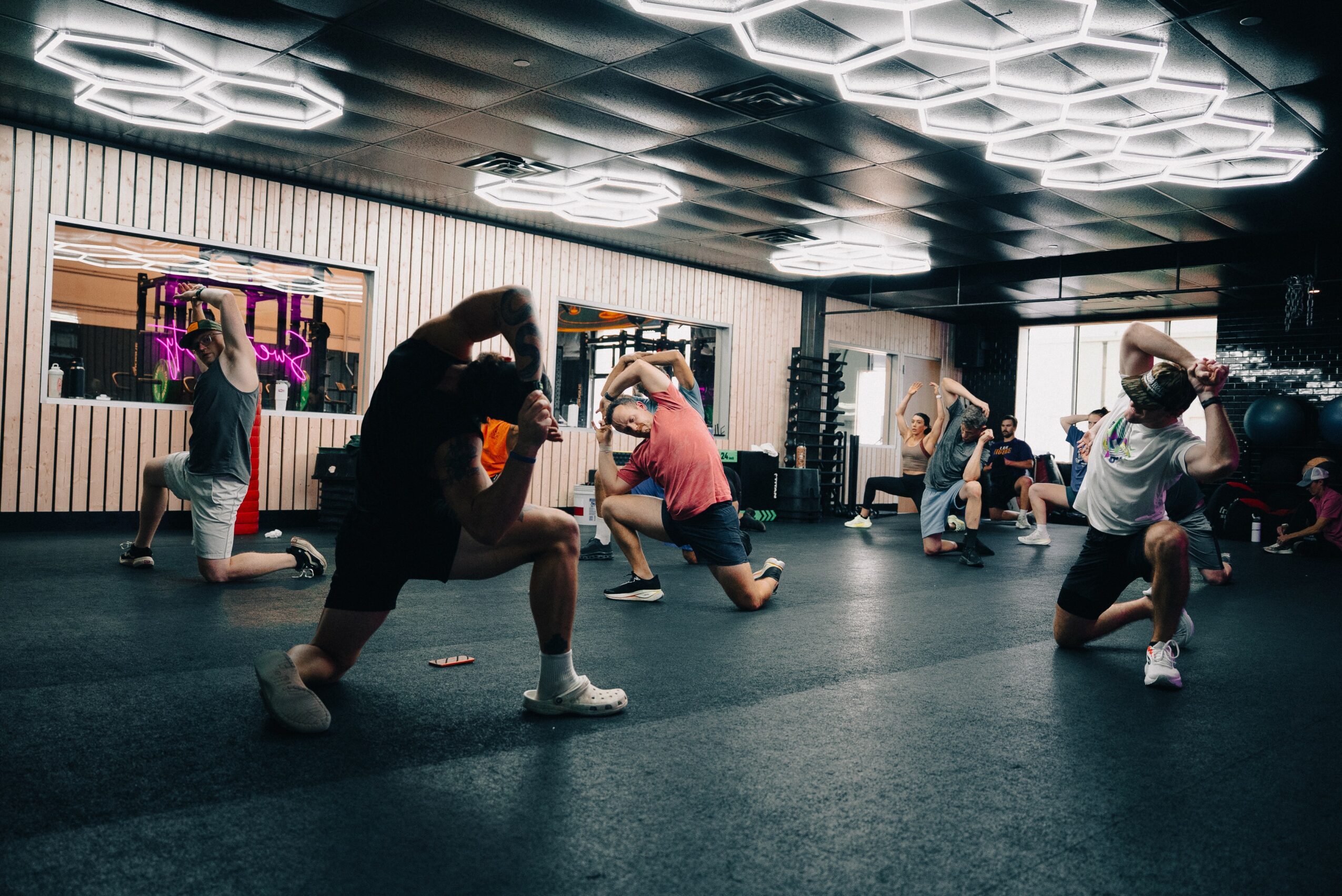 People practicing boxing in a gym with modern ceiling lights and mirrors, some wearing gloves and protective gear.