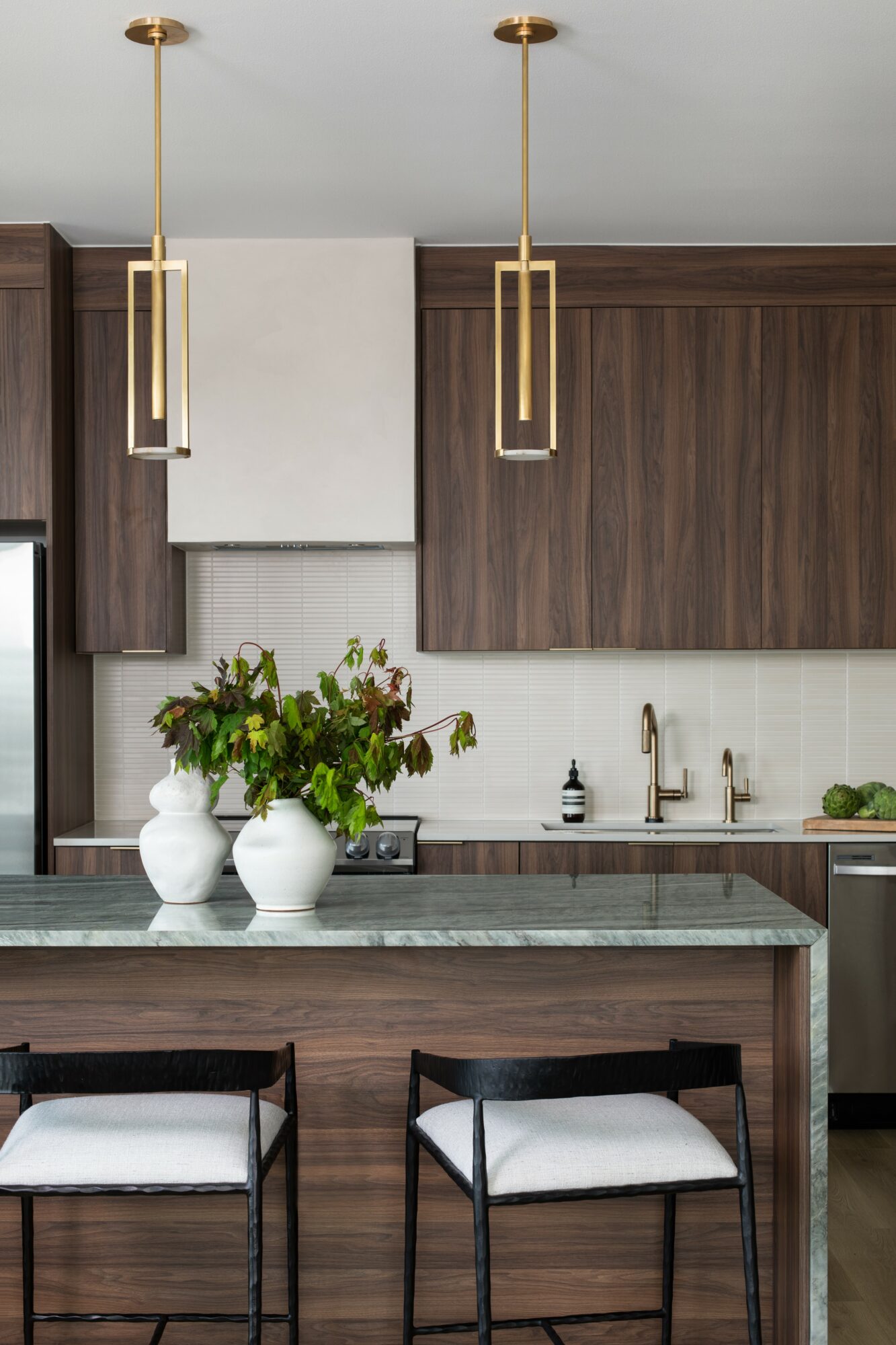 Kitchen with dark wood cabinets, two pendant lights, a green marble countertop, and two chairs with white cushions.