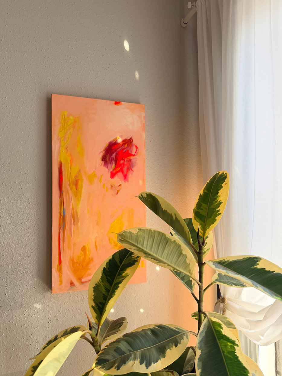 Abstract painting with pink, yellow, and red colors hanging on a wall near a window with white curtains, and a green plant in the foreground.
