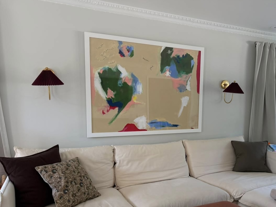Living room with a large abstract painting above a beige sofa, two wall-mounted lamps, and curtains on the right side.