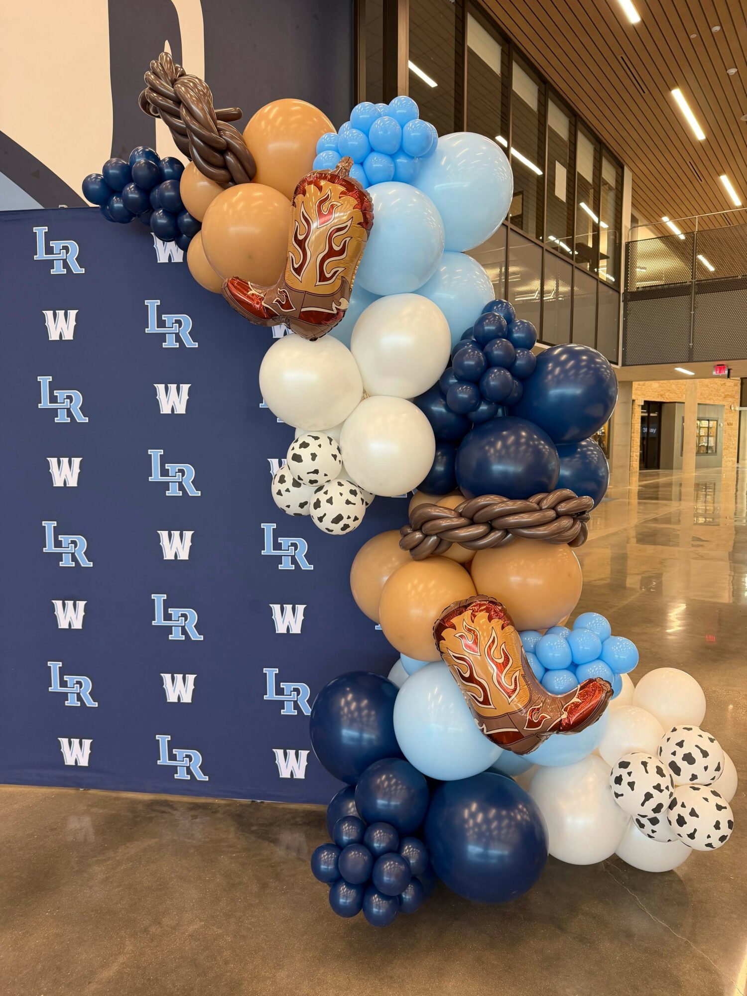 Arrangement of various balloons including blue, white, beige, and patterned ones, on a blue surface with white logos, in an indoor setting.