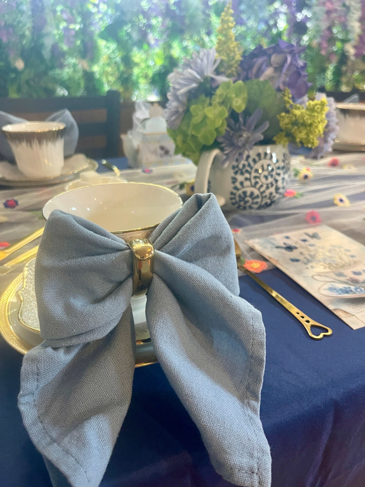 Close-up of a table setting with a large fabric bow napkin holder, floral centerpiece, and tableware, in a decorated setting.