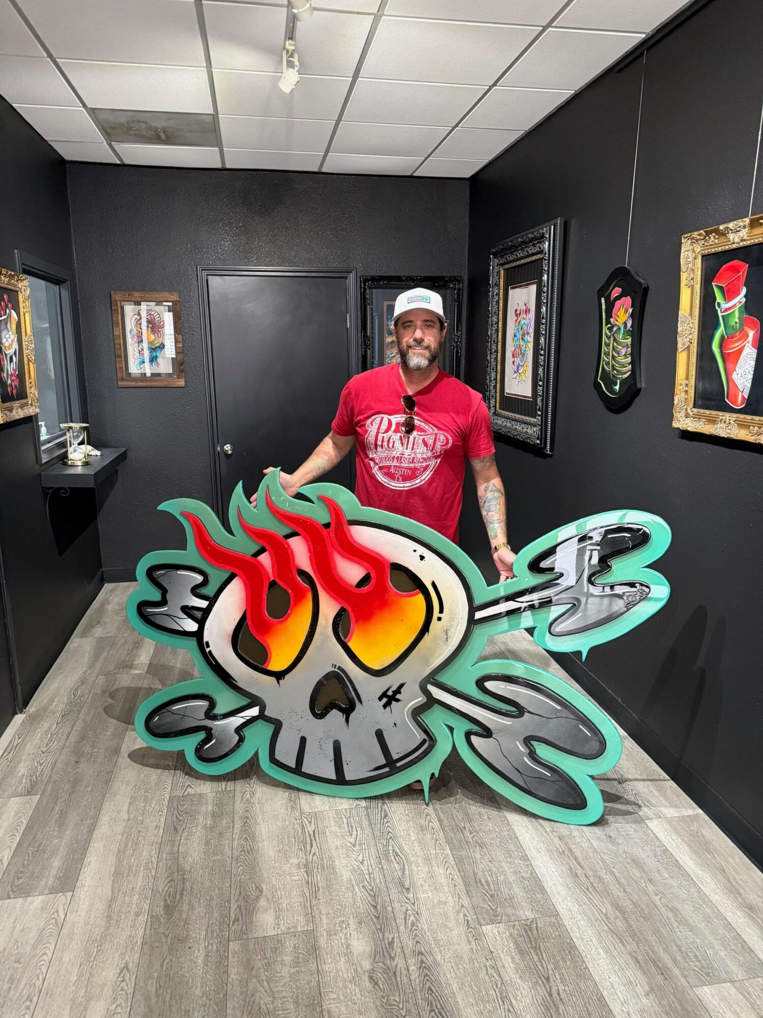 Person in red shirt standing next to a colorful clock sculpture in an indoor gallery space.