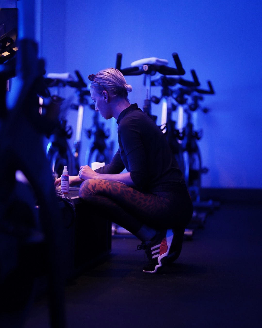 Person sitting on the floor in a dimly lit room with exercise bikes in the background, blue lighting, and a chessboard.