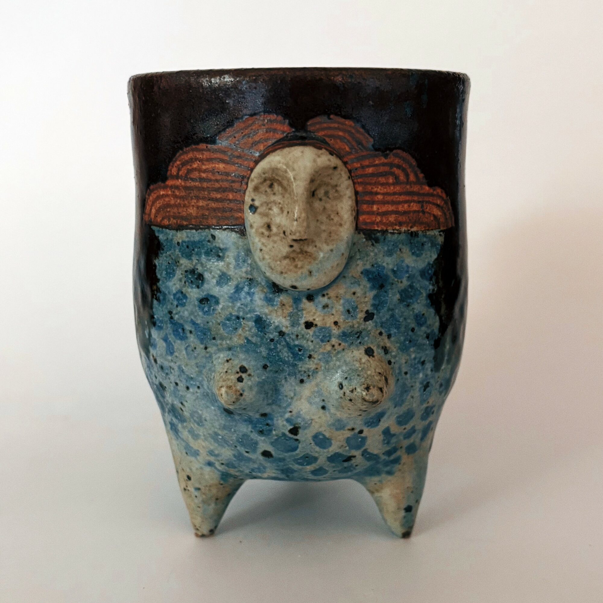 Ceramic cup with a face, moon, clouds, and water design, three-legged, on a white background.