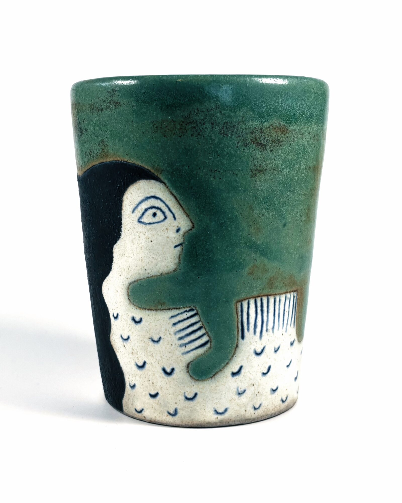 Ceramic cup with a mermaid illustration, featuring a green background and a white mermaid with black hair, facing right.